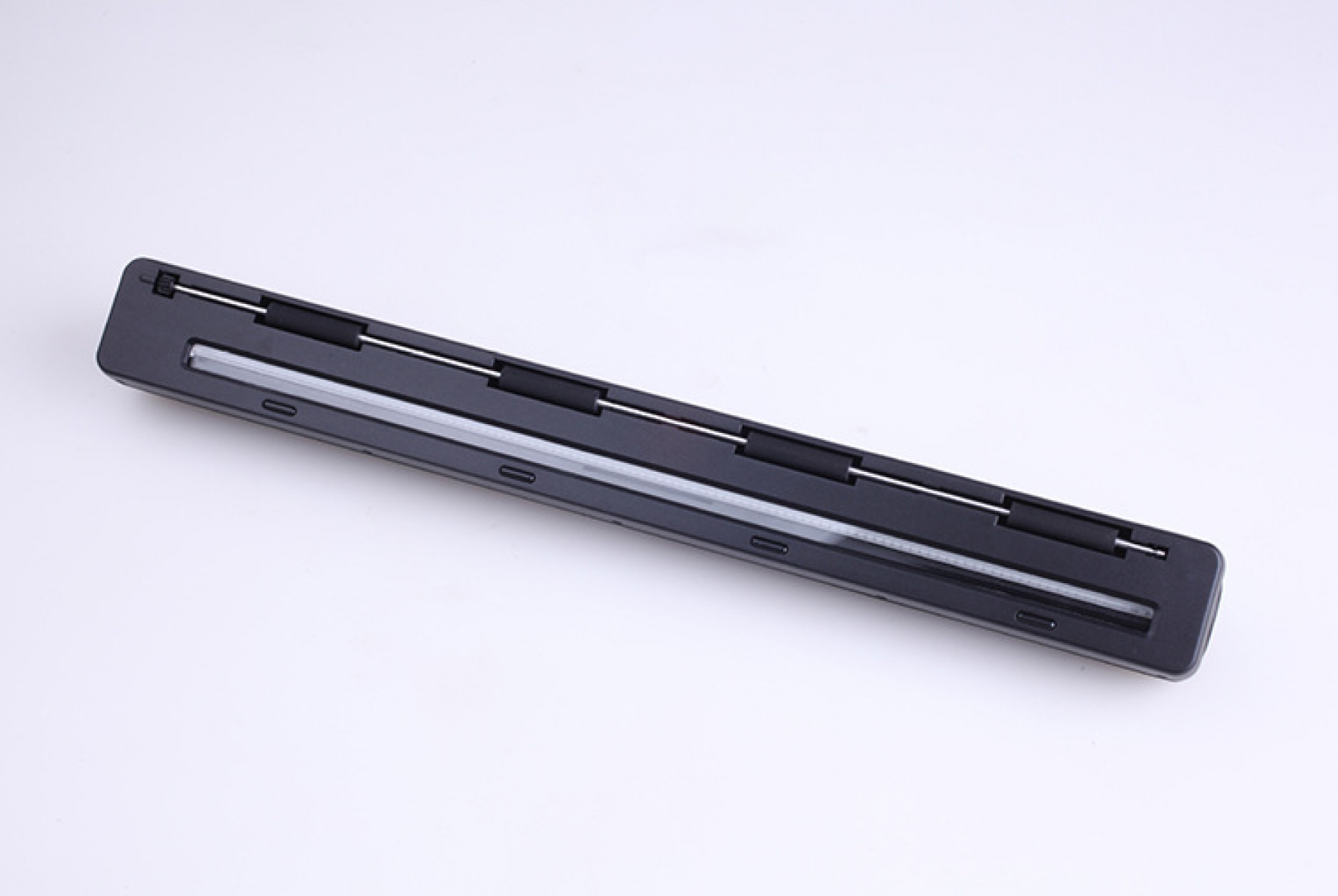 Ein schwarzer, rechteckiger Scanner liegt auf einer weißen Oberfläche. Er hat einen klaren, dünnen Lichtstreifen und silberne Metallstäbe.
