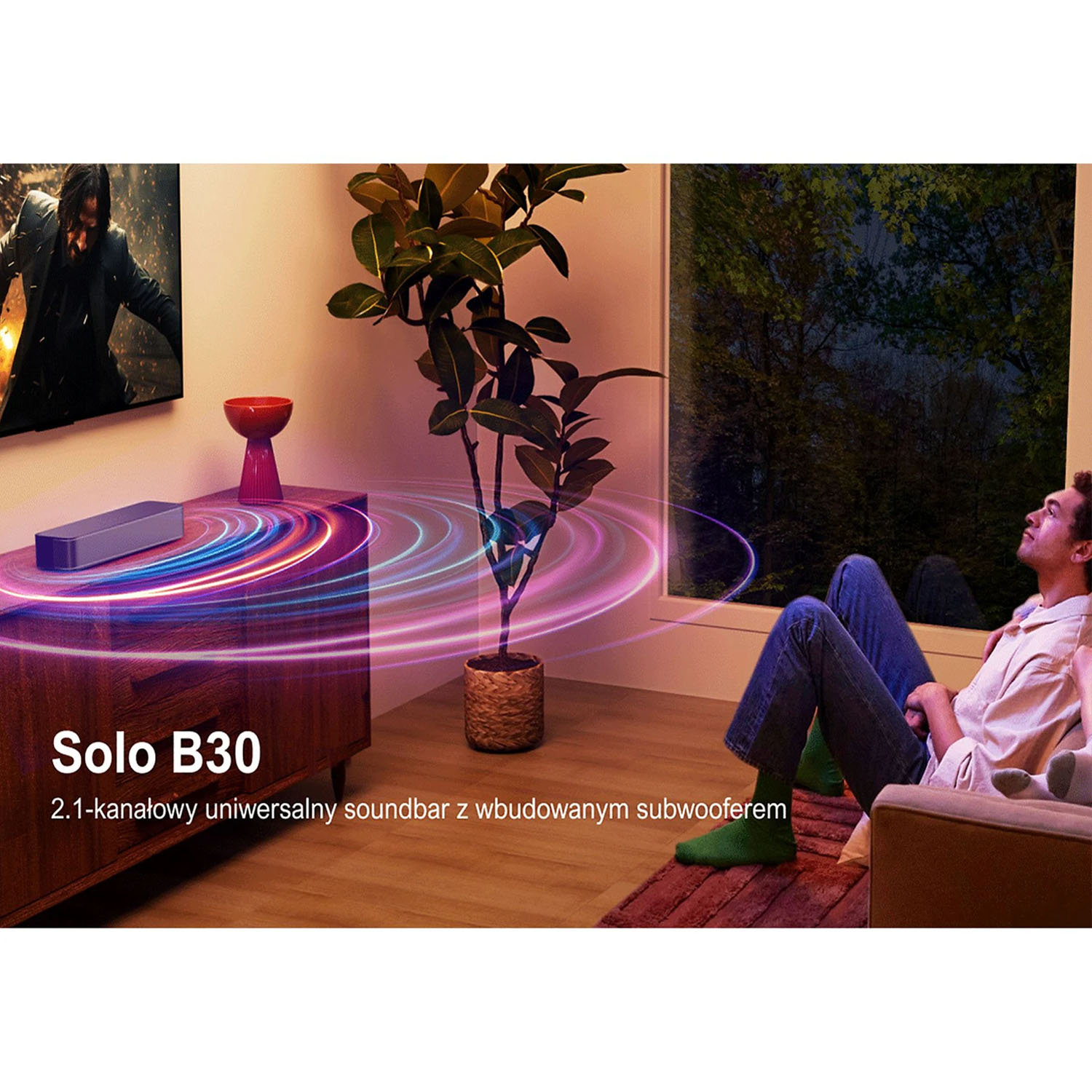 Mężczyzna ogląda telewizję, soundbar i roślina są w pokoju. Okno pokazuje drzewa. Pokój jest ciepło oświetlony.