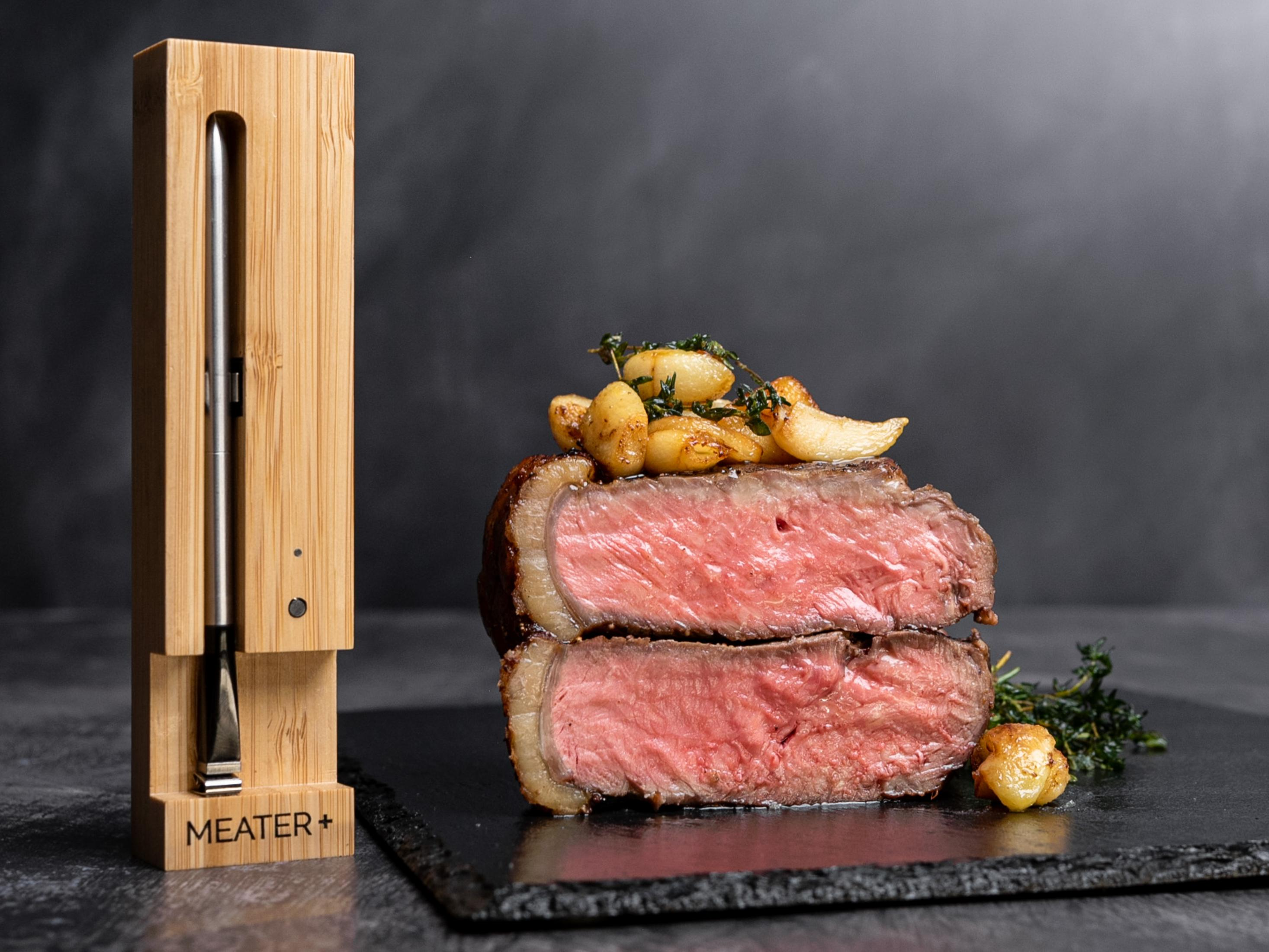 Geschnittenes Steak mit geröstetem Knoblauch, Thymian und Thermometer auf schwarzem Schiefer, dunkler Hintergrund.