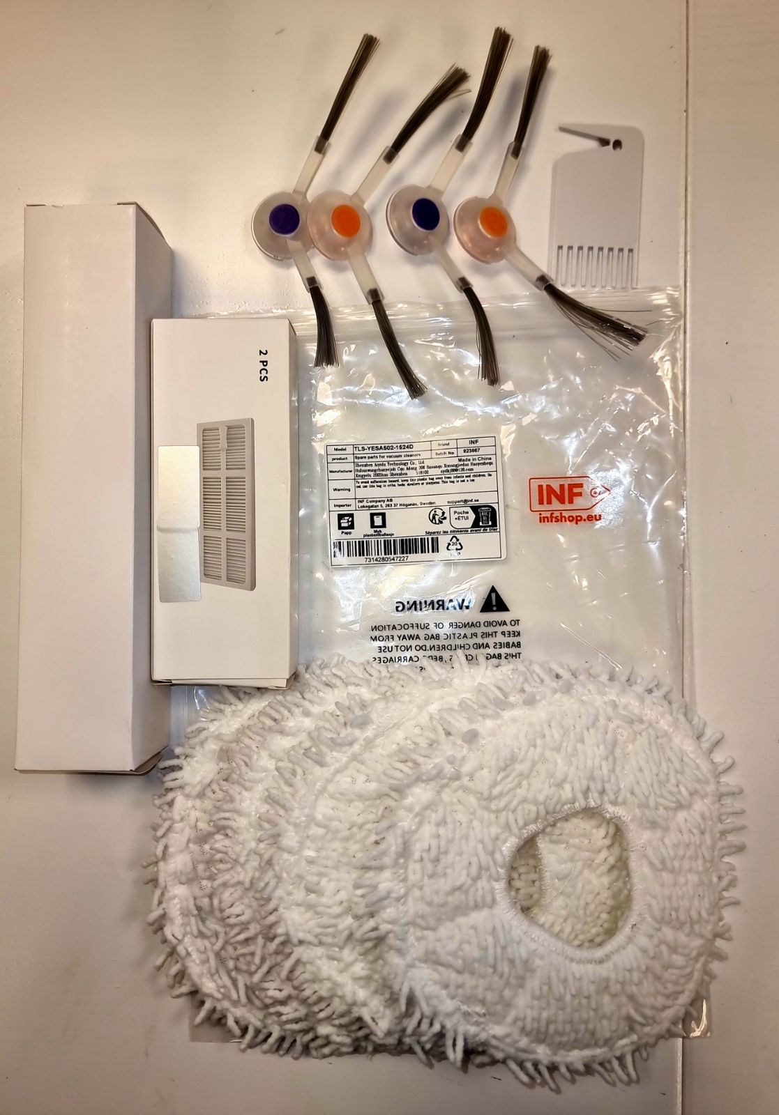 Części do odkurzacza: szczotki, grzebień, białe pudełko i biała podkładka z mikrofibry, wszystko na białej powierzchni.