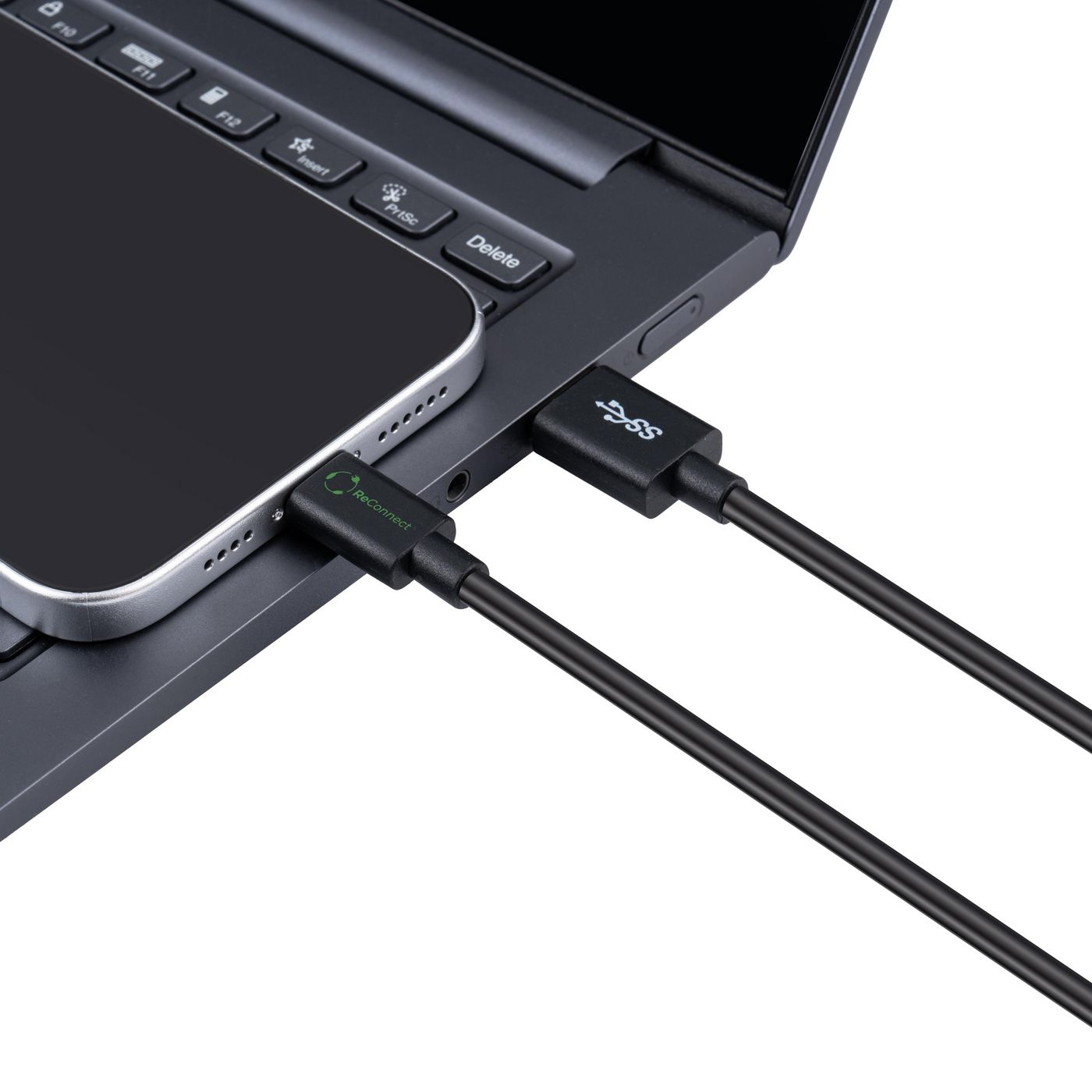 Un smartphone est connecté à un ordinateur portable via un câble de charge noir. Le clavier et l'écran de l'ordinateur portable sont également visibles.