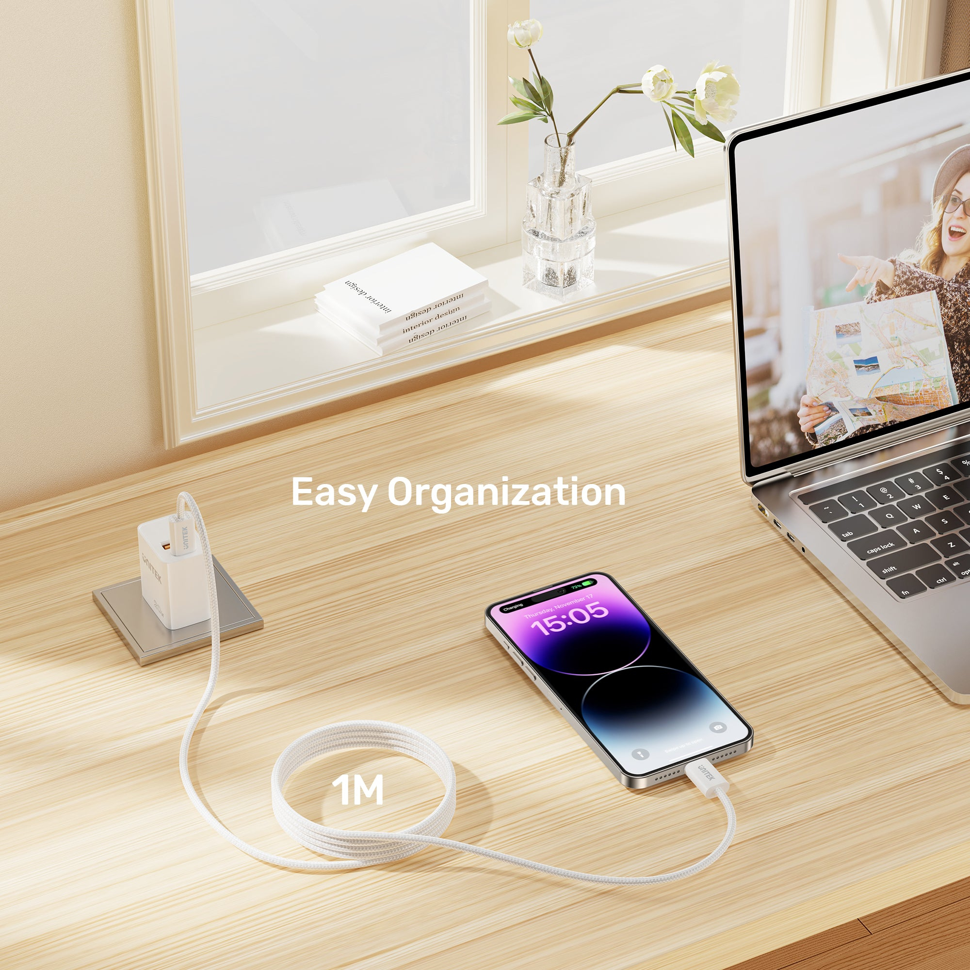 Un téléphone en charge, à côté d'un ordinateur portable. Un chargeur blanc est branché sur le téléphone, et un câble de 1M.