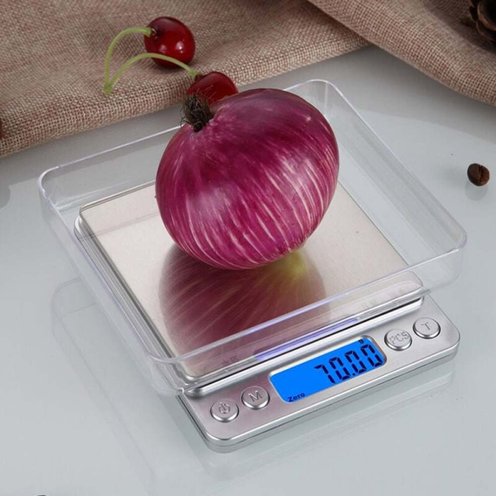 Eine rote Zwiebel liegt auf einer Digitalwaage. Zwei Kirschen befinden sich im Hintergrund, zusammen mit einem braunen Tuch und einer Kaffeebohne.