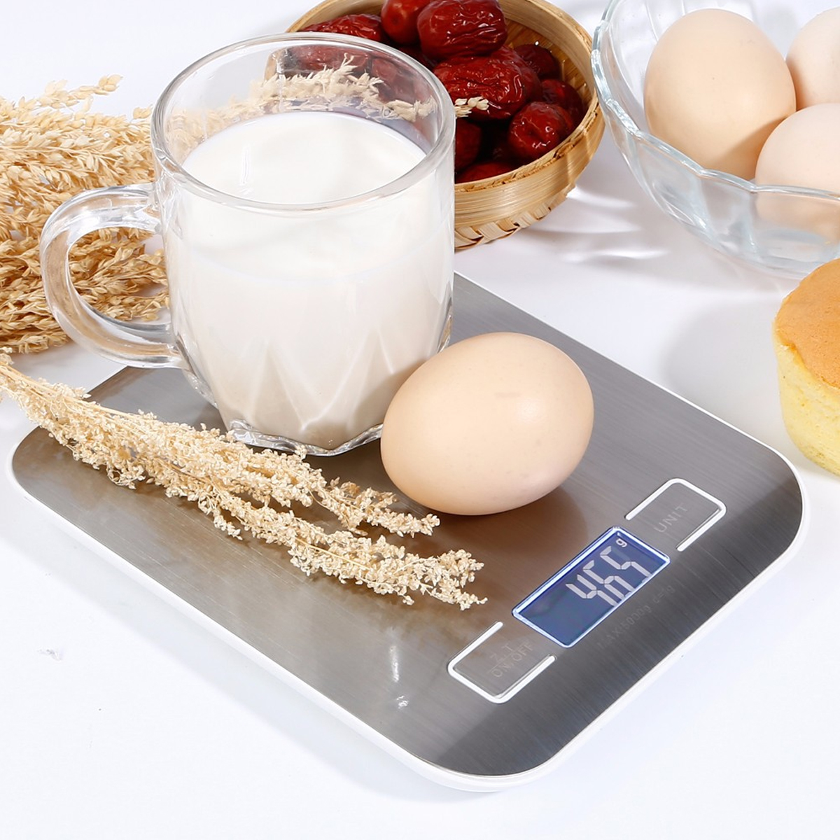Ein Ei auf einer Waage mit Milch in einem Glas, Datteln, Eier in einer Schüssel und ein kleiner Kuchen.