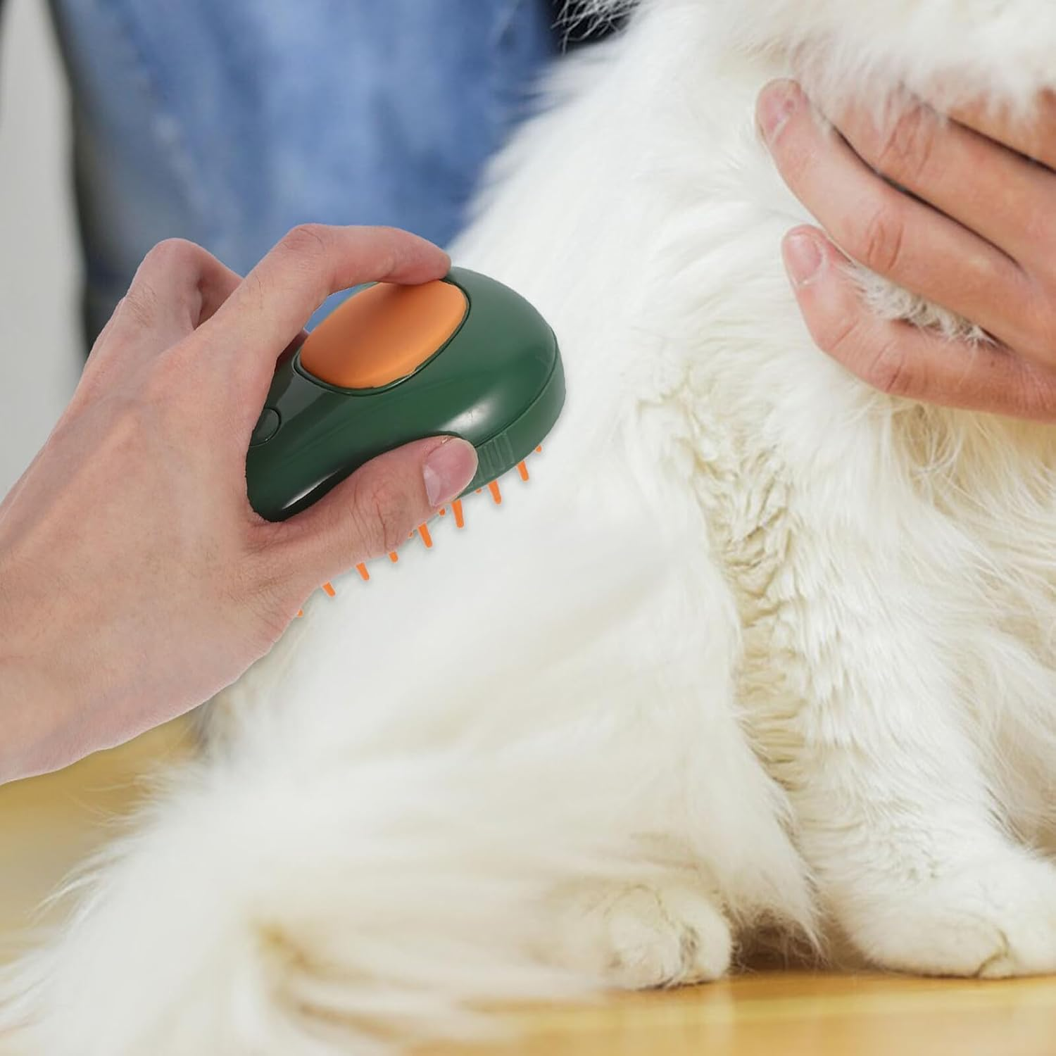 Eine Person pflegt eine flauschige weiße Katze mit einer grünen und orangenen Haustierbürste. Die Katze wird von einer anderen Person gehalten.