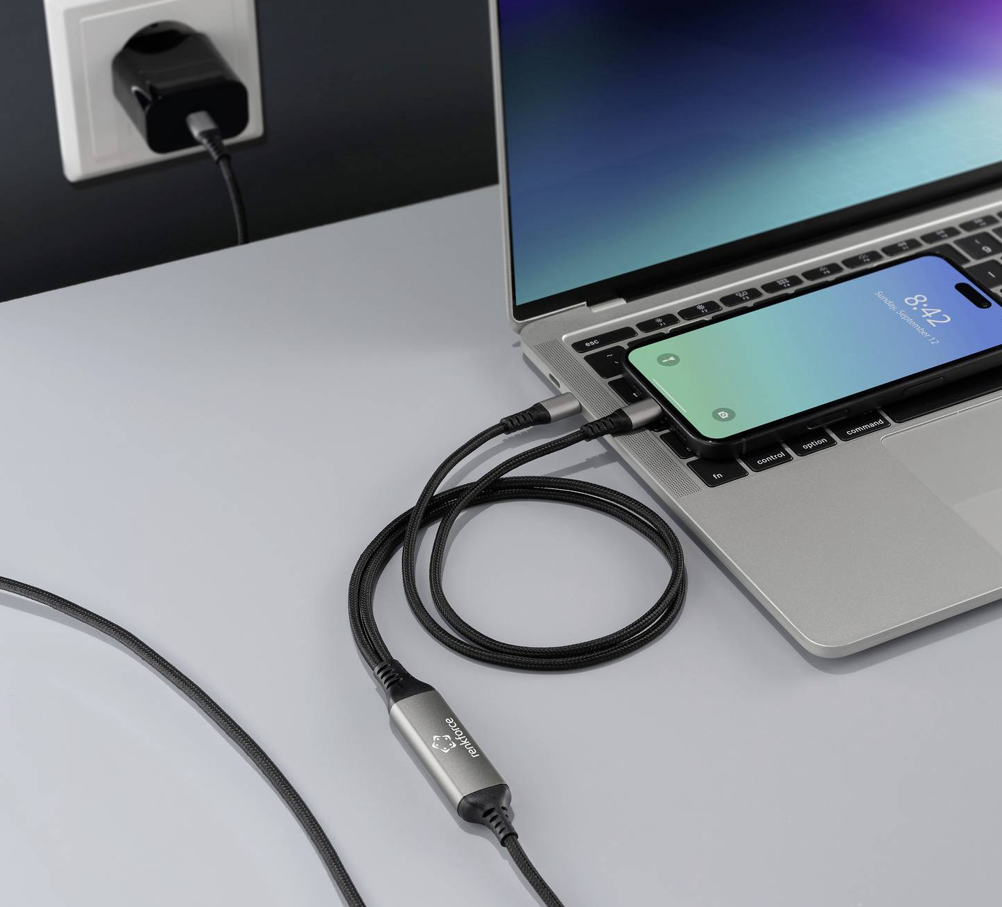Un laptop con un telefono sulla tastiera è in carica. Un cavo collega il telefono a un caricabatterie collegato a una presa a muro.