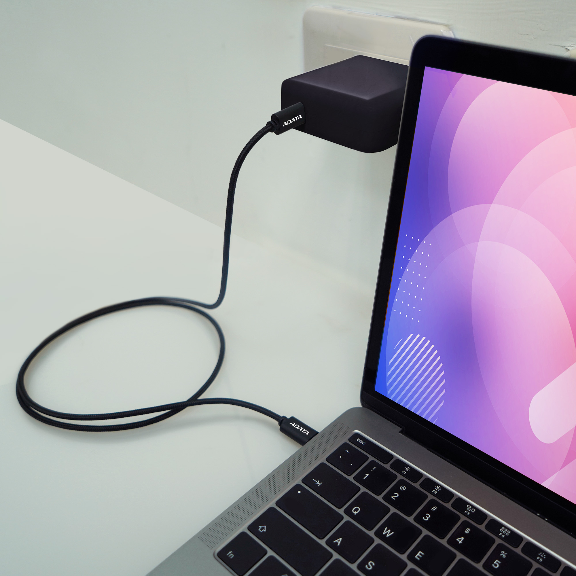 Ein Laptop ist mit einem Netzteil verbunden. Der Laptop-Bildschirm zeigt eine farbenfrohe Grafik. Ein Kabel verbindet die beiden.