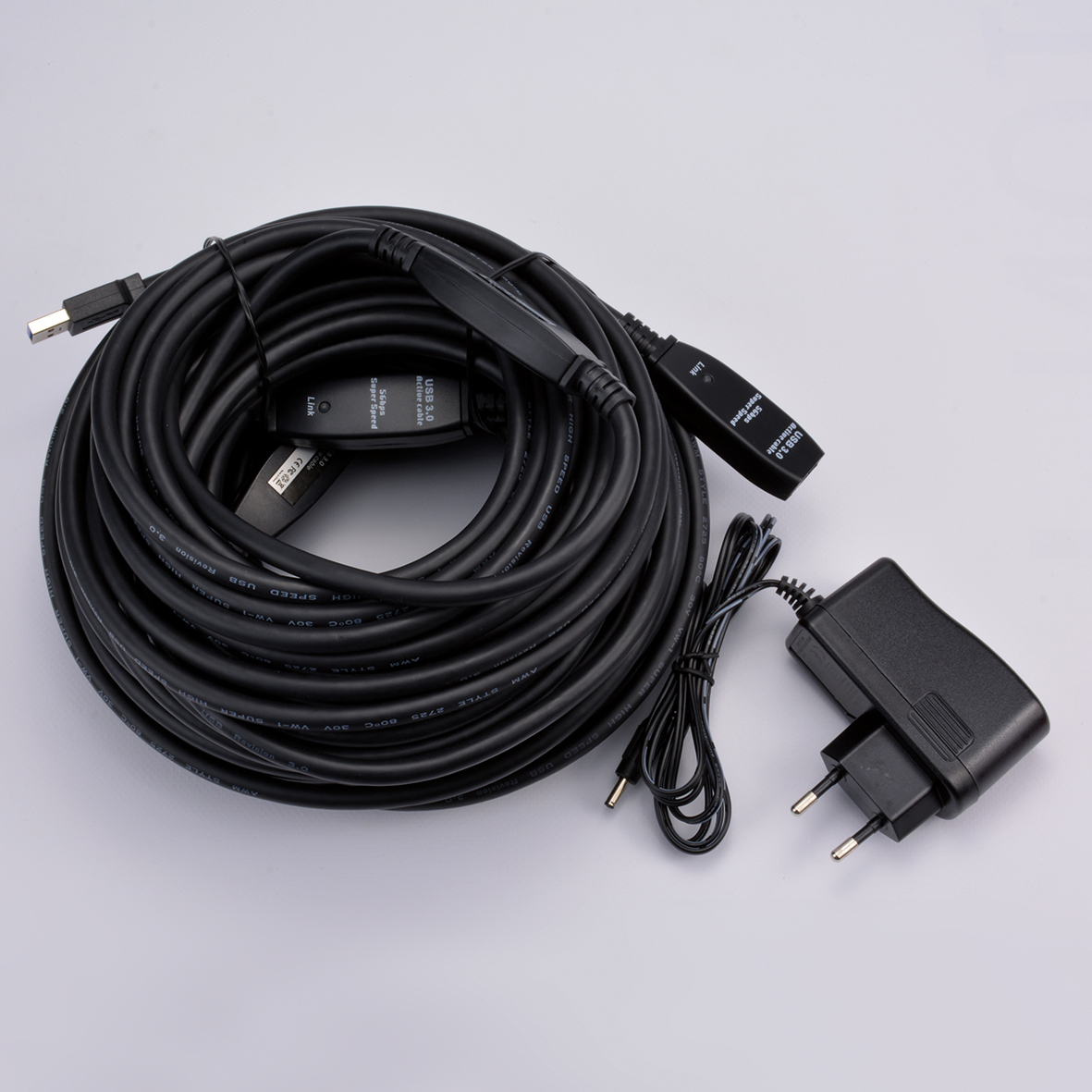 Ein schwarzes USB 3.0-Aktivkabel, aufgerollt, mit Anschlüssen und einem Netzteil. Das Kabel hat Etiketten mit Geschwindigkeit und Revision.