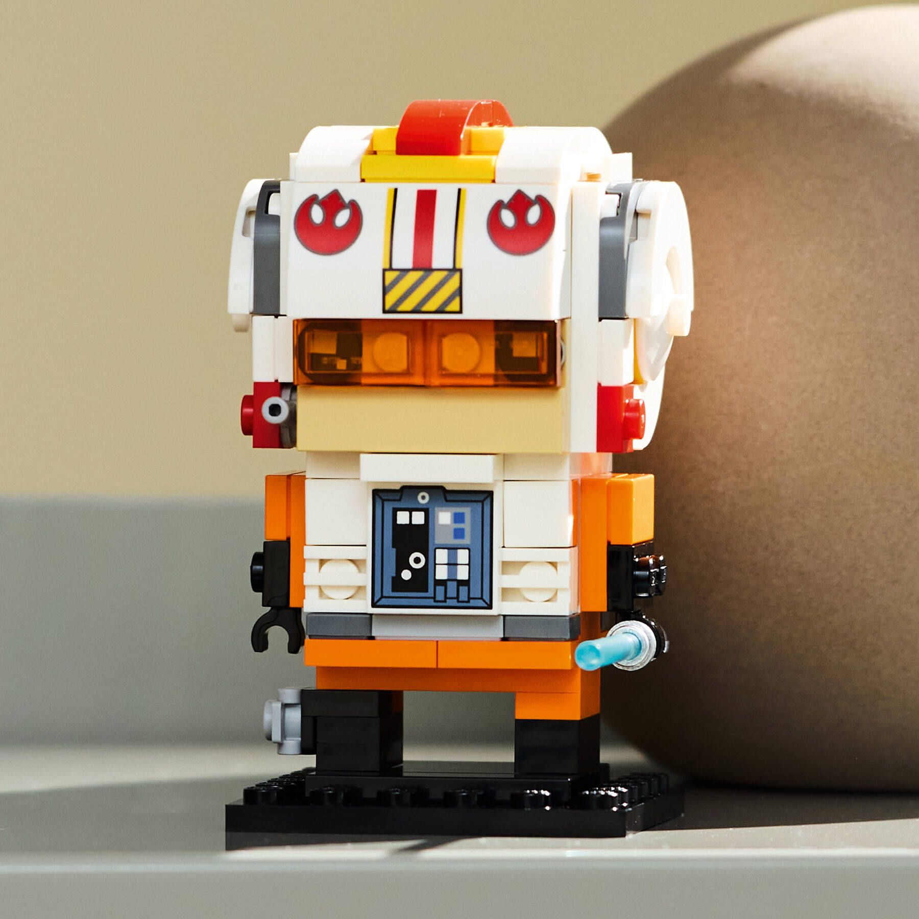 Eine Lego-Roboterfigur mit weißen, orangefarbenen und schwarzen Teilen. Es hat einen roten Streifen und ein Logo mit blauem Zubehör.