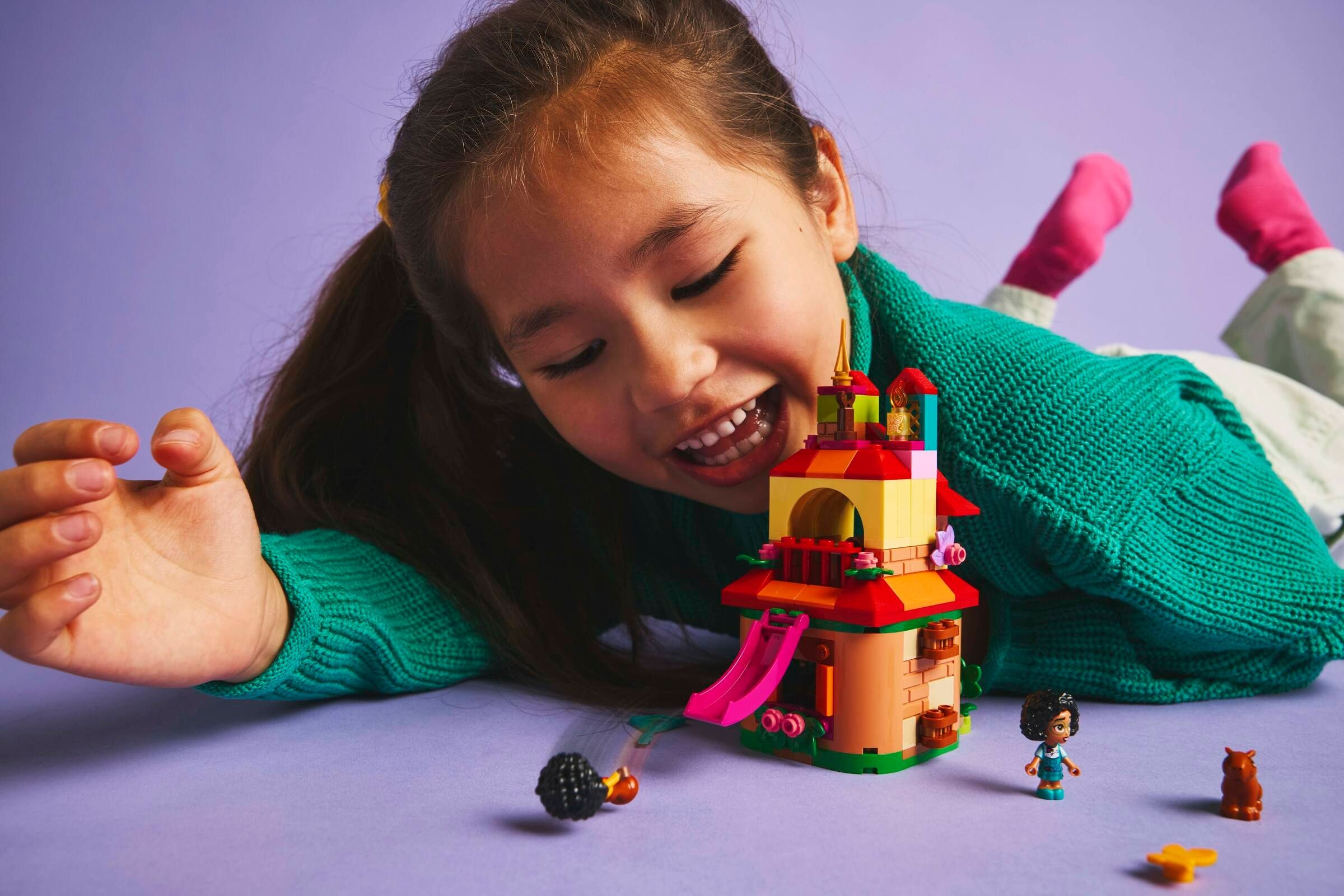 Ein Mädchen betrachtet ein Lego-Schloss. Das Schloss hat eine Rutsche. Eine Minifigur und ein Bär stehen daneben.