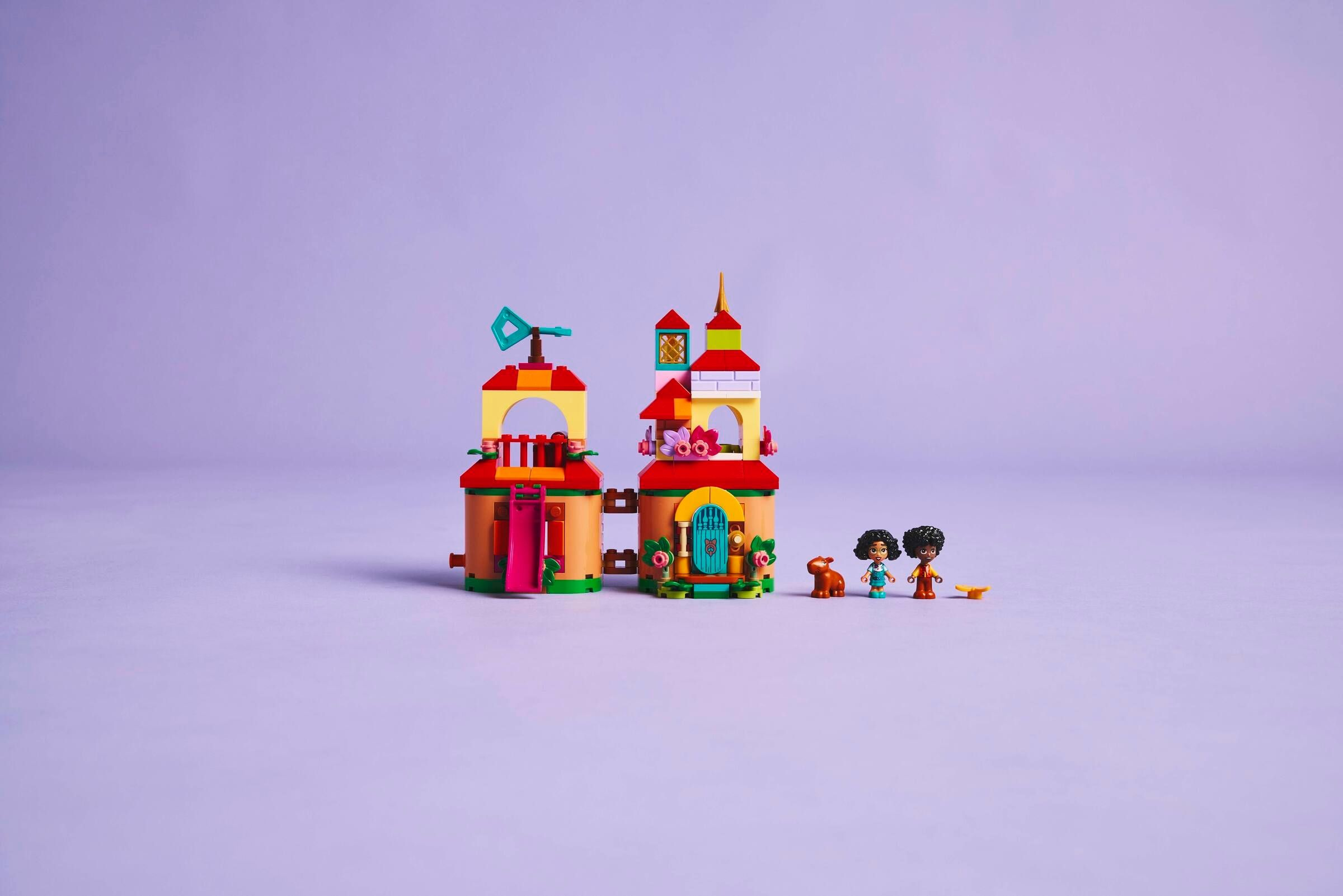Lego-Set mit bunten Gebäuden, zwei Figuren und einem braunen Tier auf lila Hintergrund.