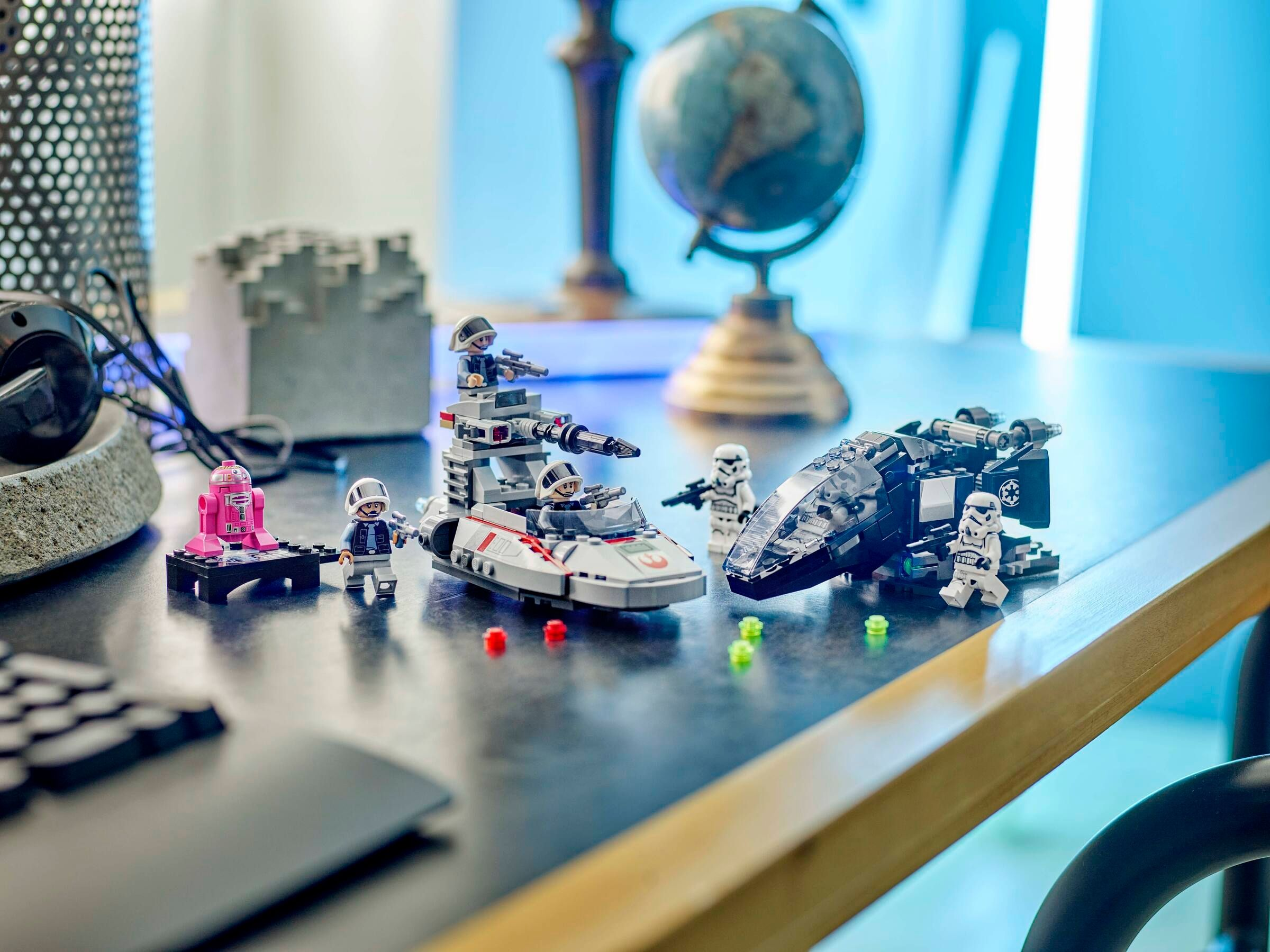 Scena LEGO Star Wars na biurku z modelami statków, figurkami, różowym robotem, globusem i słuchawkami.
