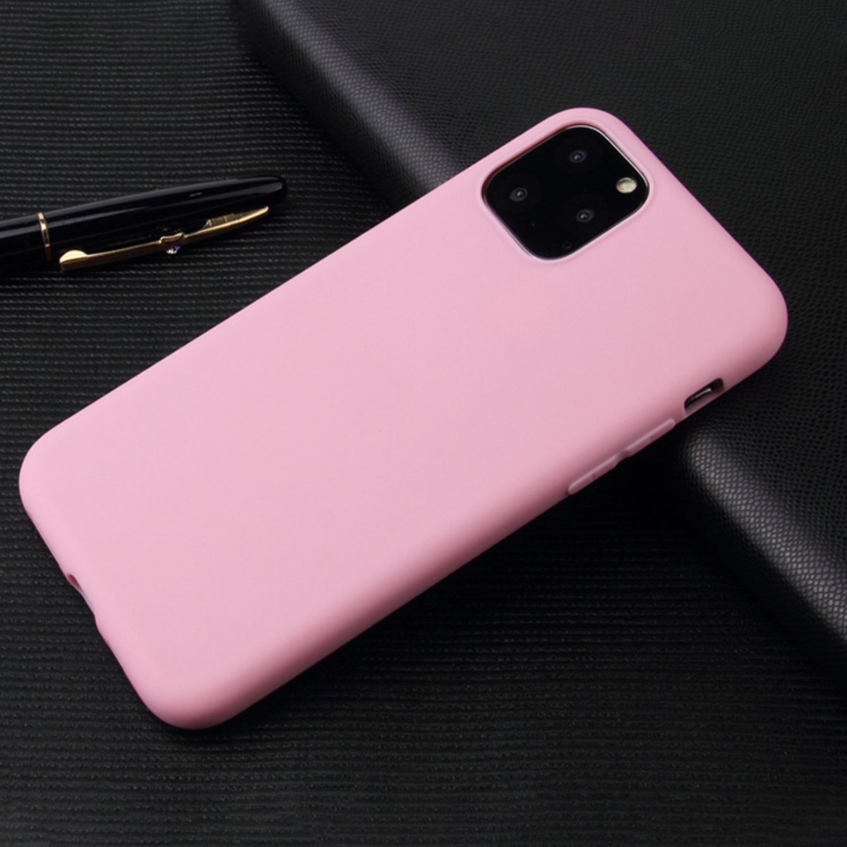 Eine rosa Handyhülle auf einer strukturierten schwarzen Oberfläche. Im Hintergrund befindet sich ein Stift. Die Hülle hat mehrere Kameralinsen.