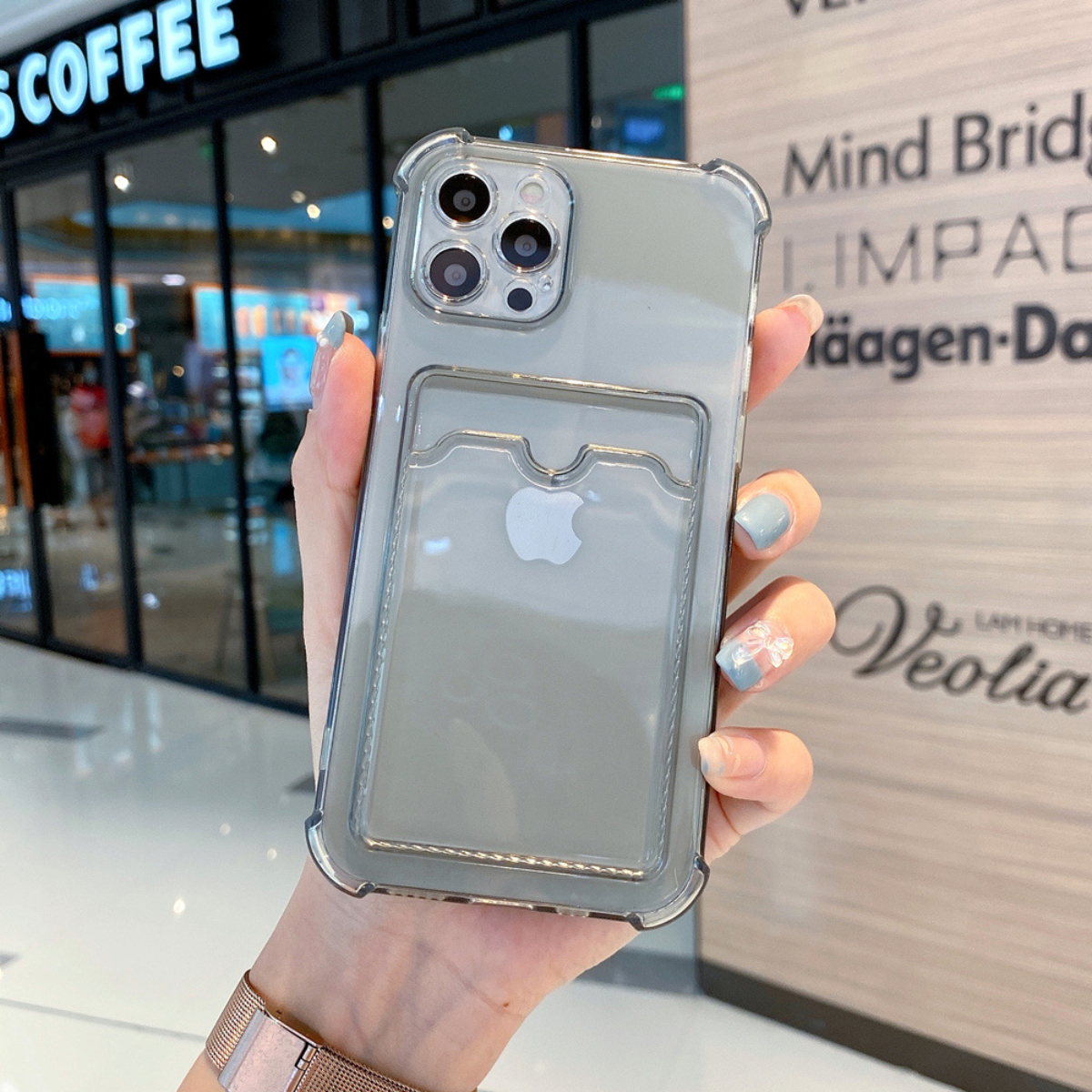 Eine Hand hält eine transparente Handyhülle mit einem iPhone darin. Die Hülle hat einen Kartenhalter. Der Hintergrund ist ein Geschäft.