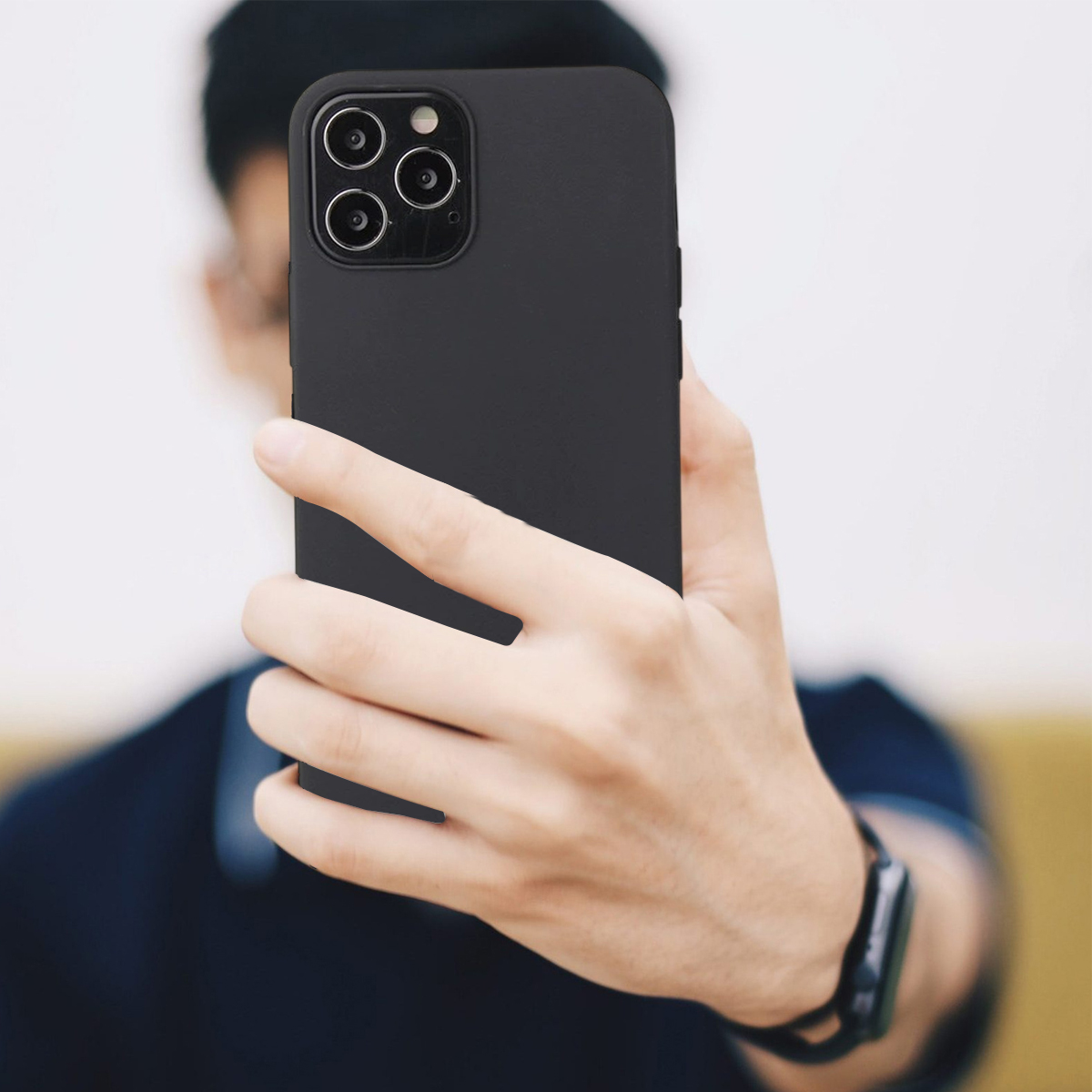 Eine Person hält ein schwarzes Smartphone und macht ein Selfie. Das Telefon hat drei Kameras. Die Person trägt ein dunkelblaues Hemd.