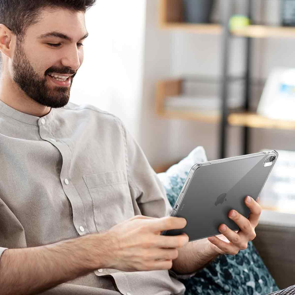 Ein Mann mit Bart lächelt, während er ein Tablet hält. Er sitzt auf einem Sofa, und im Hintergrund sind Regale.