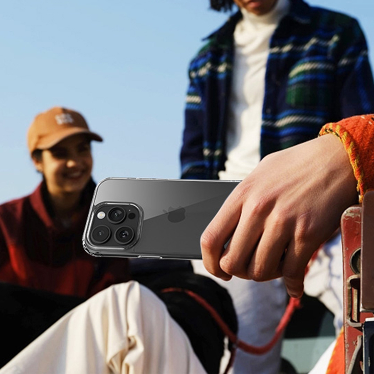 Eine Person hält ein Telefon, andere sind im Hintergrund unscharf. Das Telefon ist klar und hat eine Kamera. Menschen tragen Freizeitkleidung.