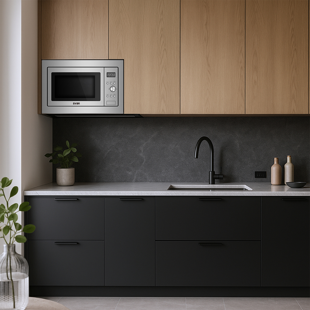 Cocina moderna con microondas, armarios negros y fregadero. Armarios superiores de madera y encimera con plantas y botellas.