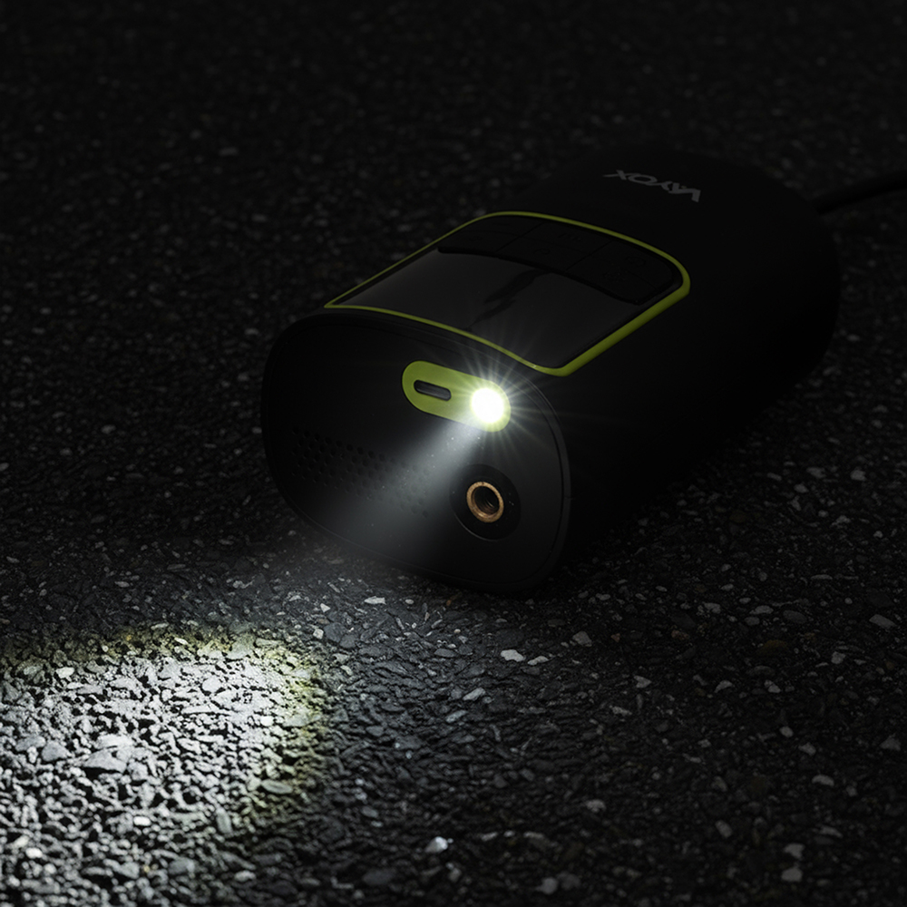 Czarne urządzenie z jasnym światłem na ciemnej powierzchni asfaltu. Urządzenie ma zielony akcent. Światło świeci na ziemię.