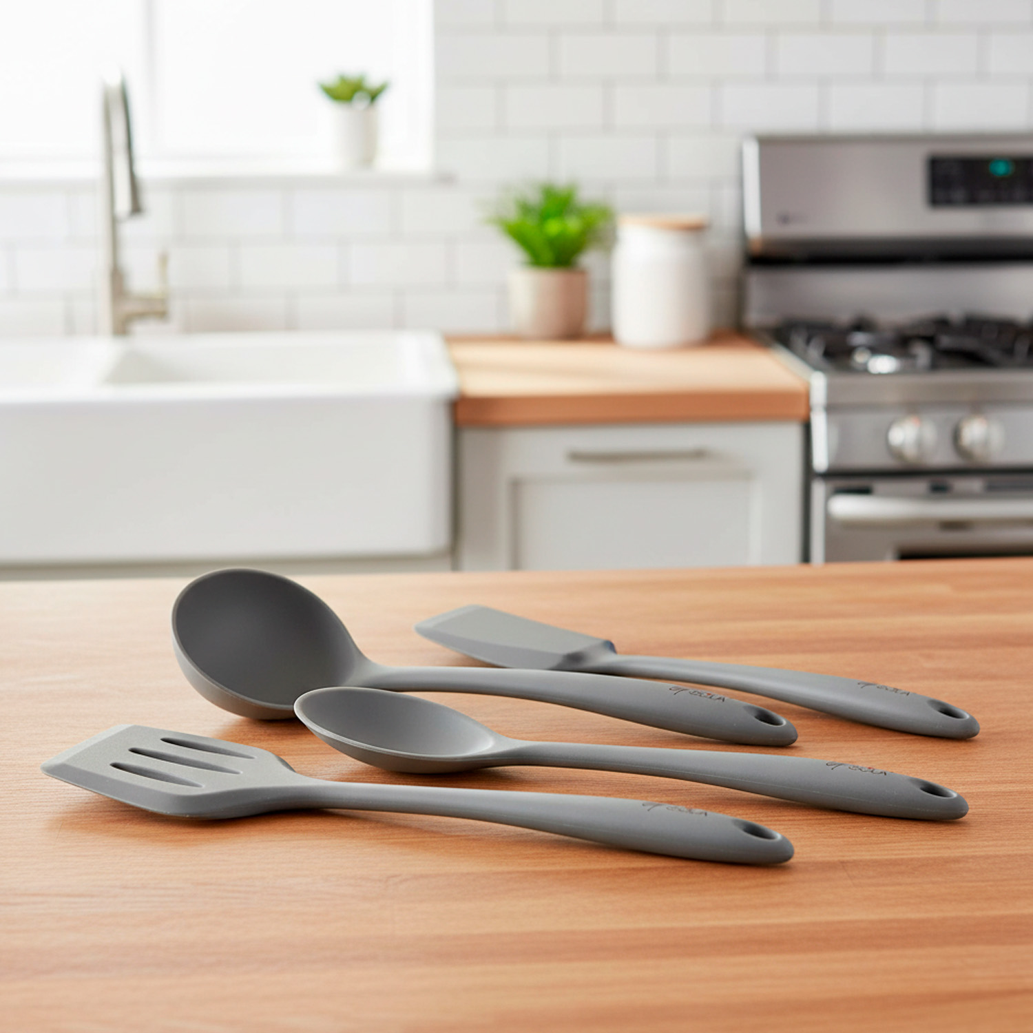 Cuatro utensilios de cocina grises sobre una superficie de madera: cucharón, espátula, espátula ranurada y cuchara. Fondo de cocina visible.