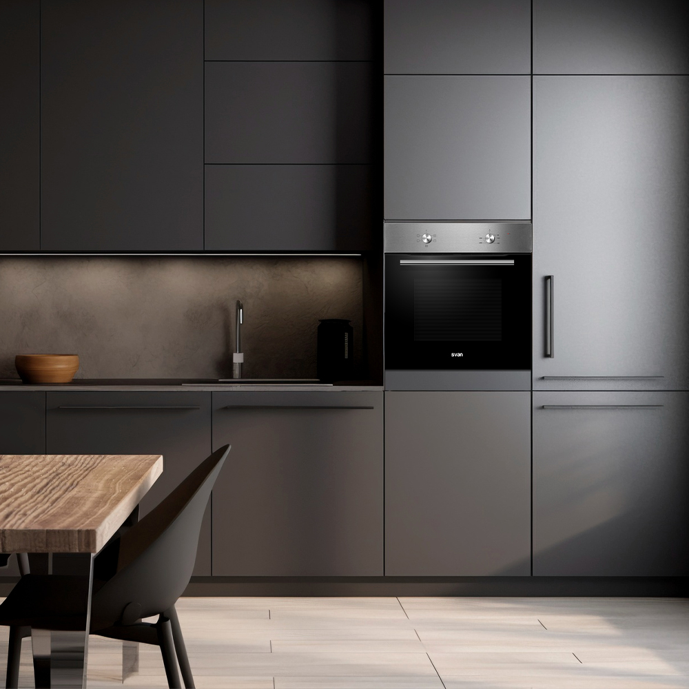 Cocina moderna con armarios gris oscuro, horno, mesa de madera, silla negra y suelo de madera. También se ven un fregadero y un cuenco de madera.