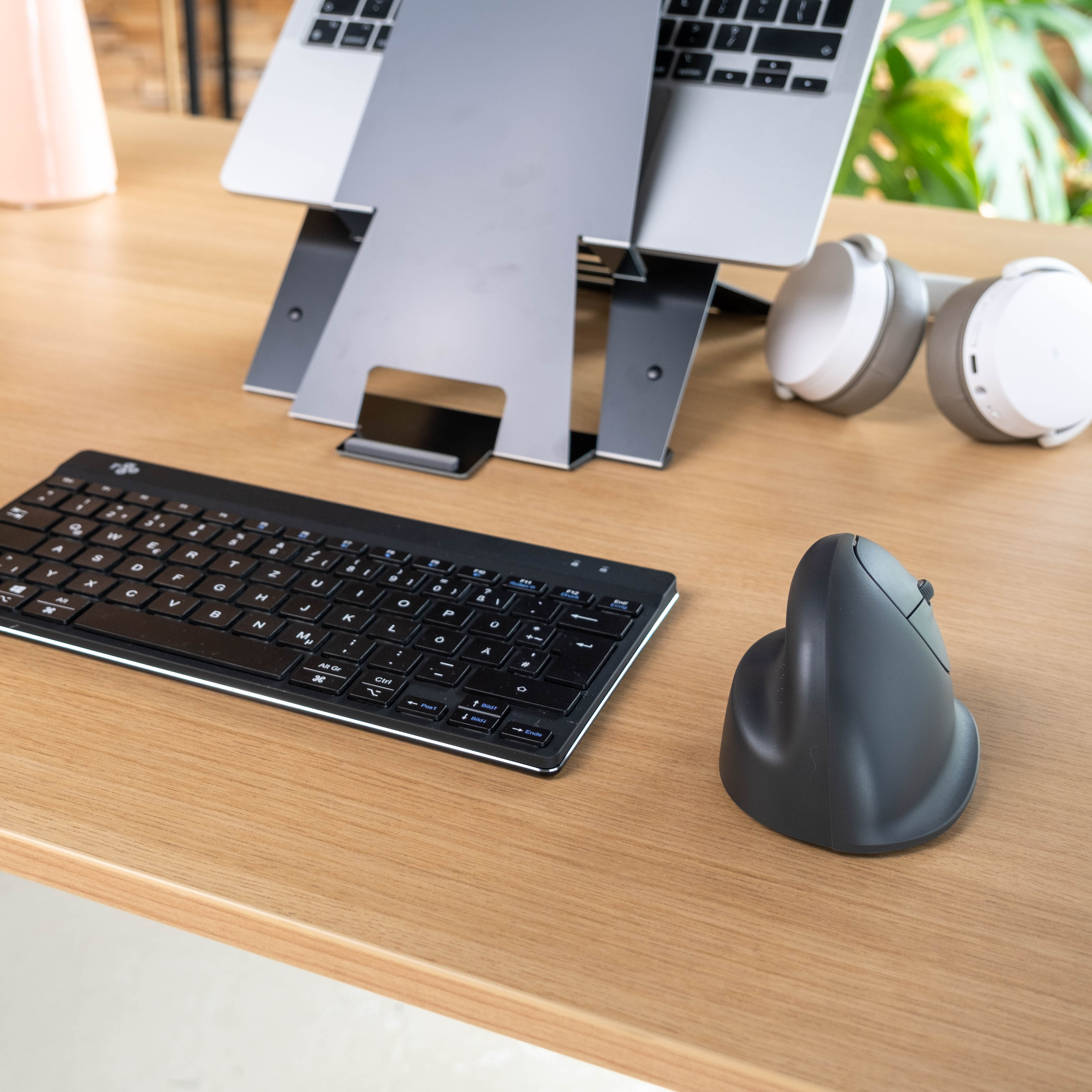Een bureau met een laptop, toetsenbord, verticale muis en koptelefoon. Het bureau is van hout.