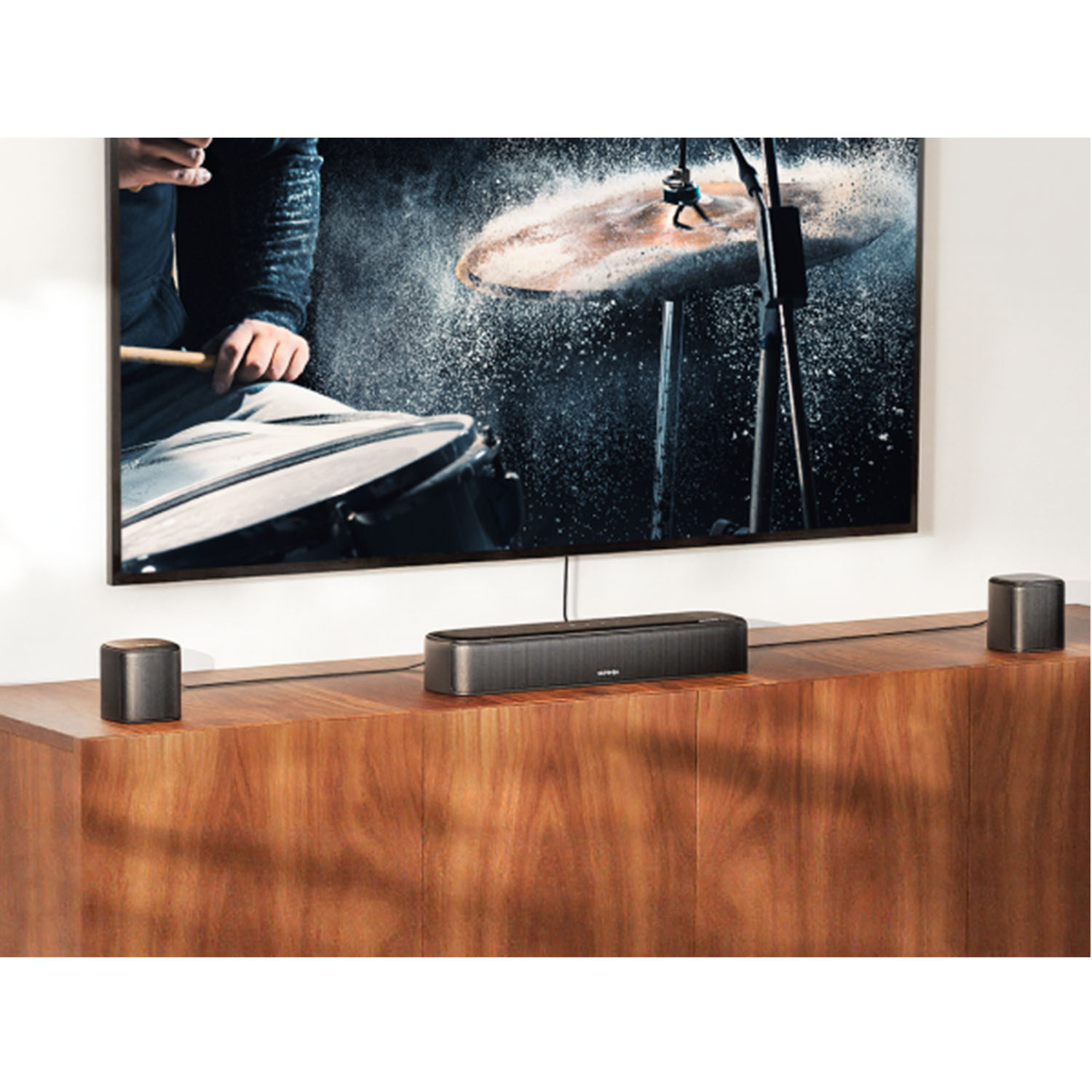 Telewizor wyświetla perkusistę. Poniżej soundbar i dwa głośniki na drewnianej szafce.