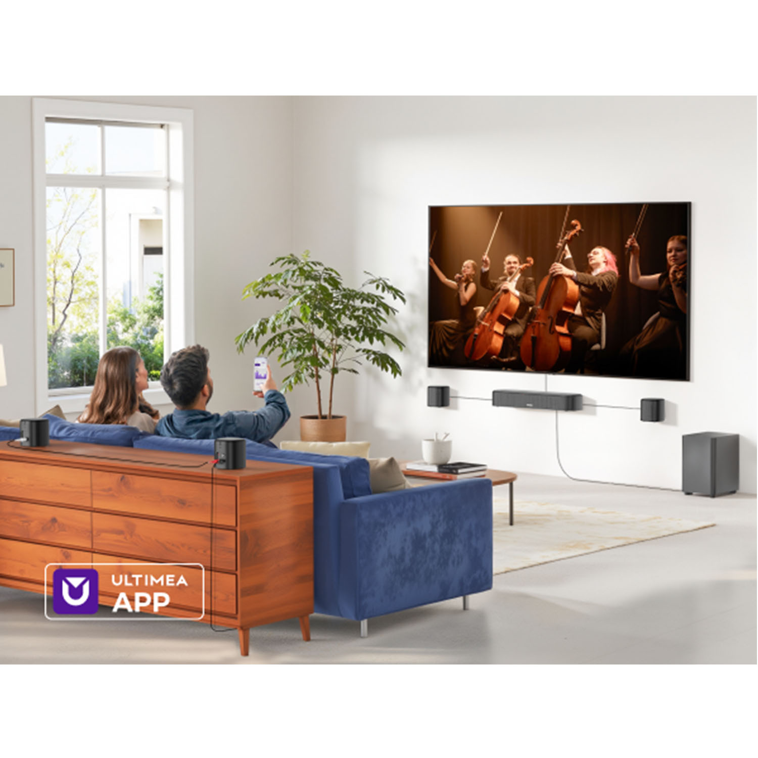 Para ogląda telewizję, która pokazuje kwartet smyczkowy. Głośniki i subwoofer otaczają niebieską kanapę i drewnianą szafkę.