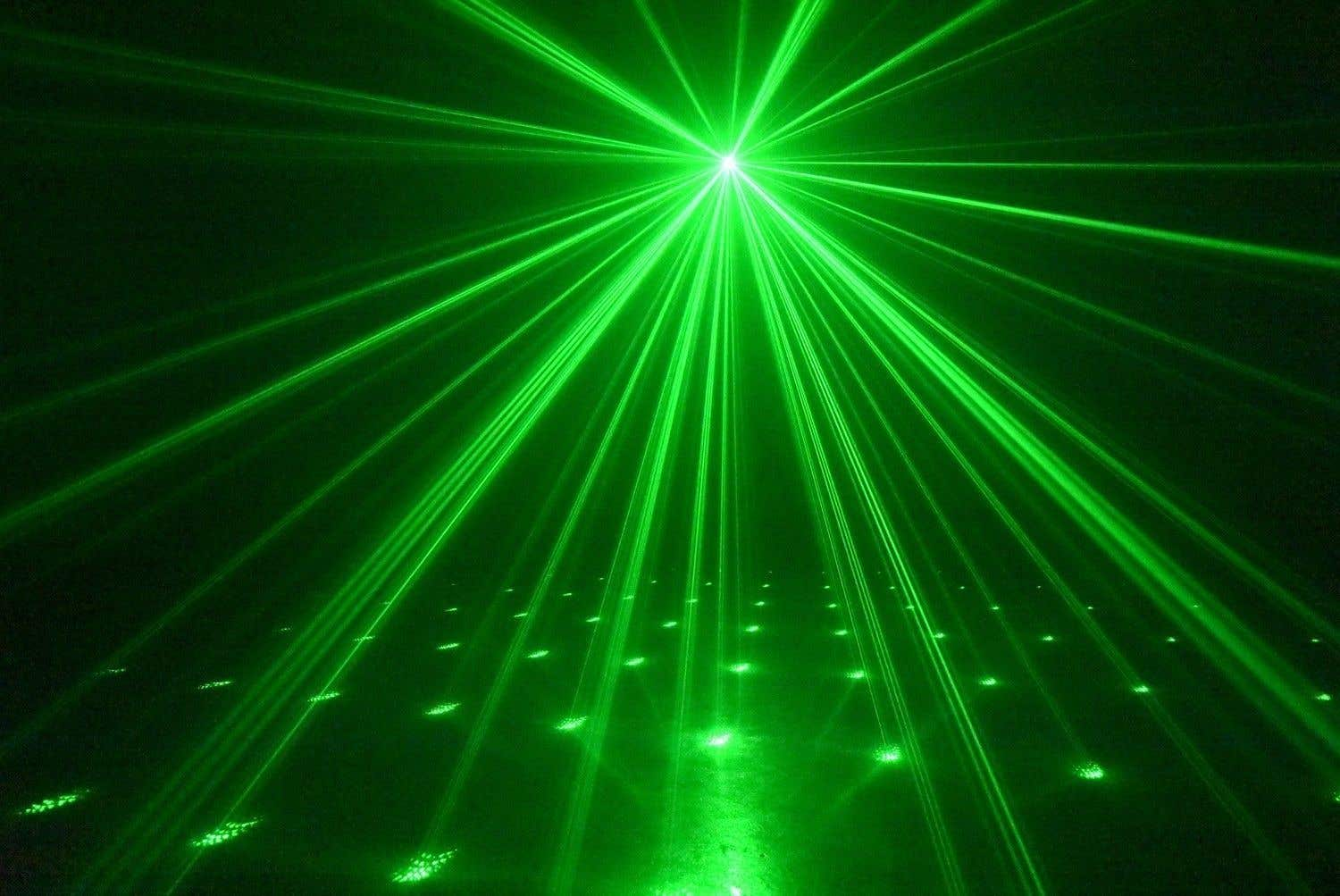 Rayos láser verdes irradian desde un punto central, iluminando un espacio oscuro. Los rayos convergen en una superficie con puntos verdes dispersos.