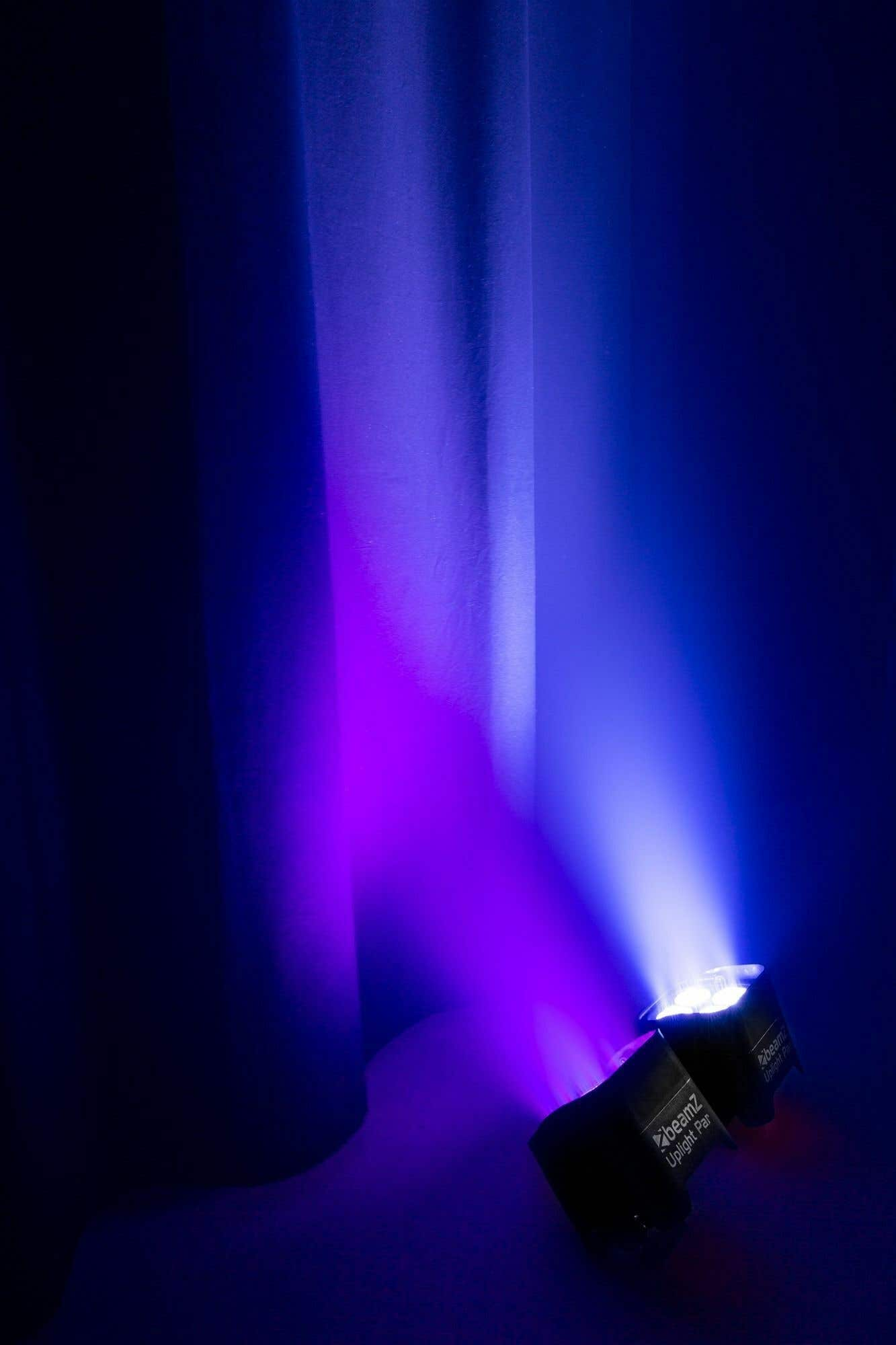 Dos focos negros proyectan luz púrpura y azul sobre un fondo azul oscuro con una cortina.