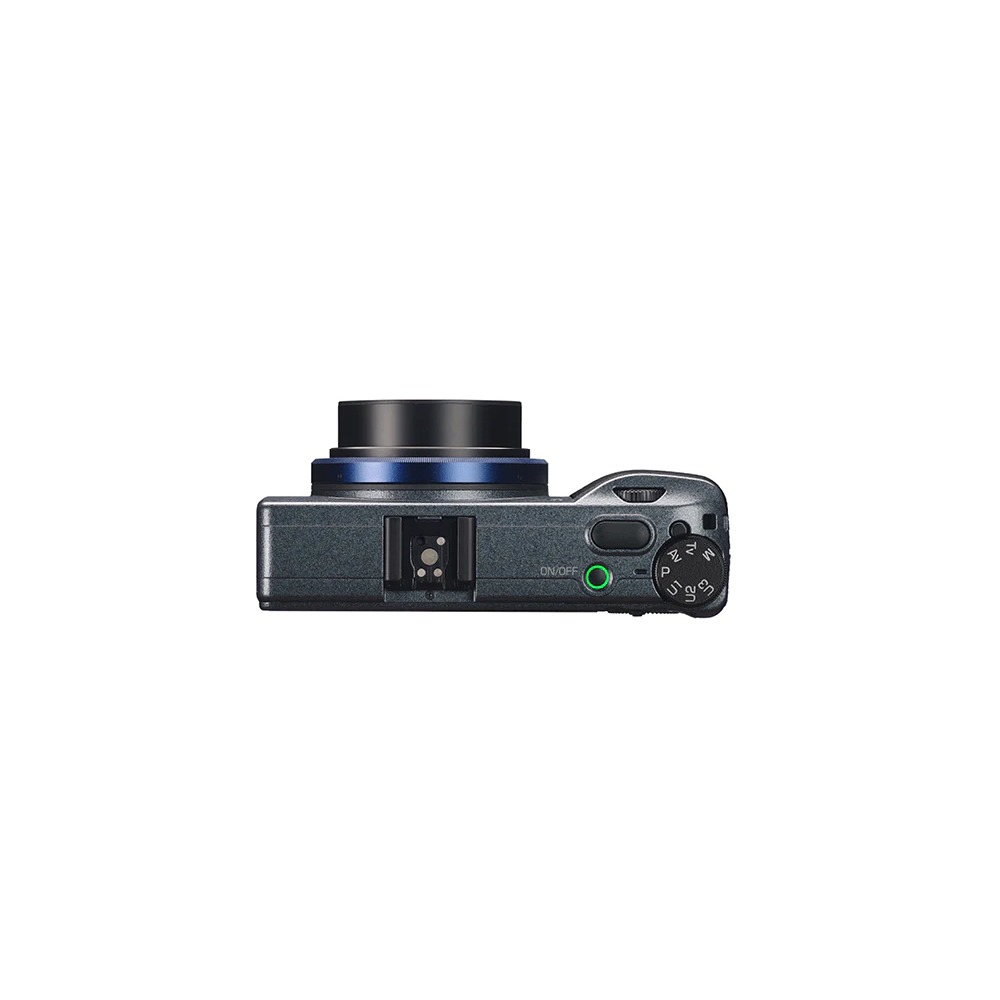 Vue de dessus d'un appareil photo numérique compact. Il a un objectif noir, un anneau bleu et un corps gris. Commandes et flash visibles.