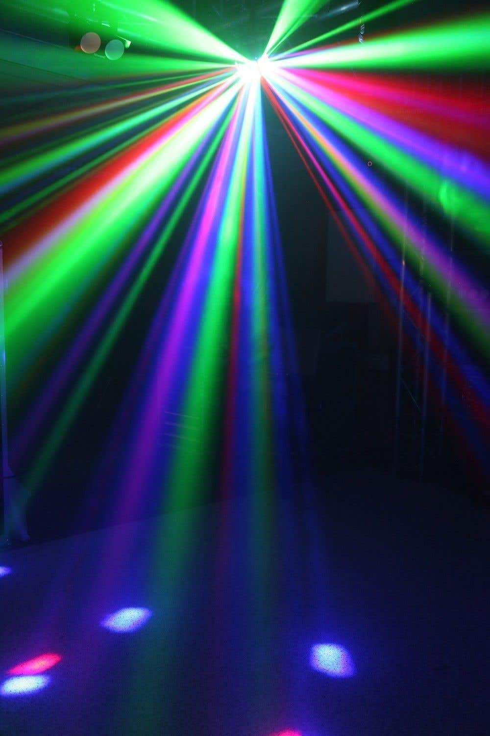 Luces de escenario coloridas crean rayos verdes, rojos, azules y morados. Las luces brillan sobre un suelo oscuro con manchas dispersas.