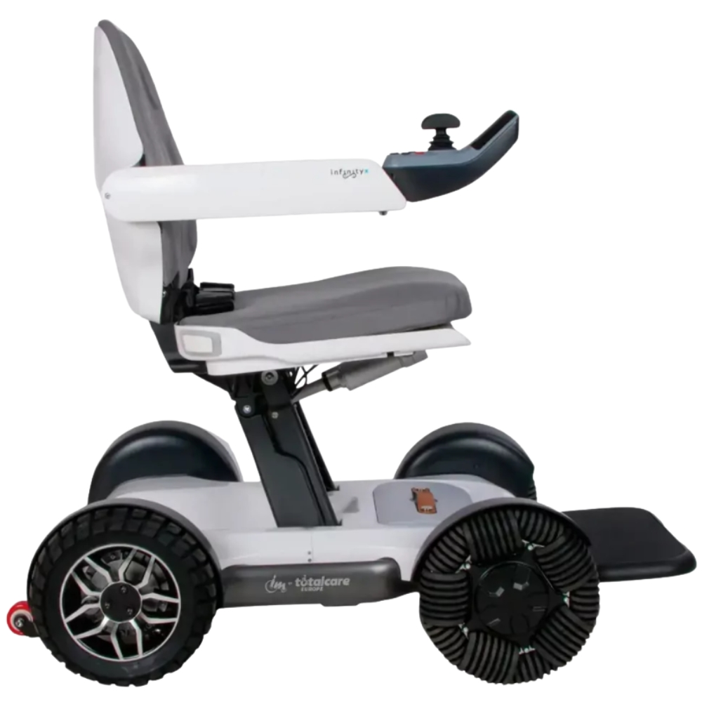 Silla de ruedas motorizada blanca y gris con ruedas negras. Tiene asiento, reposabrazos y joystick. La silla está sobre fondo blanco.