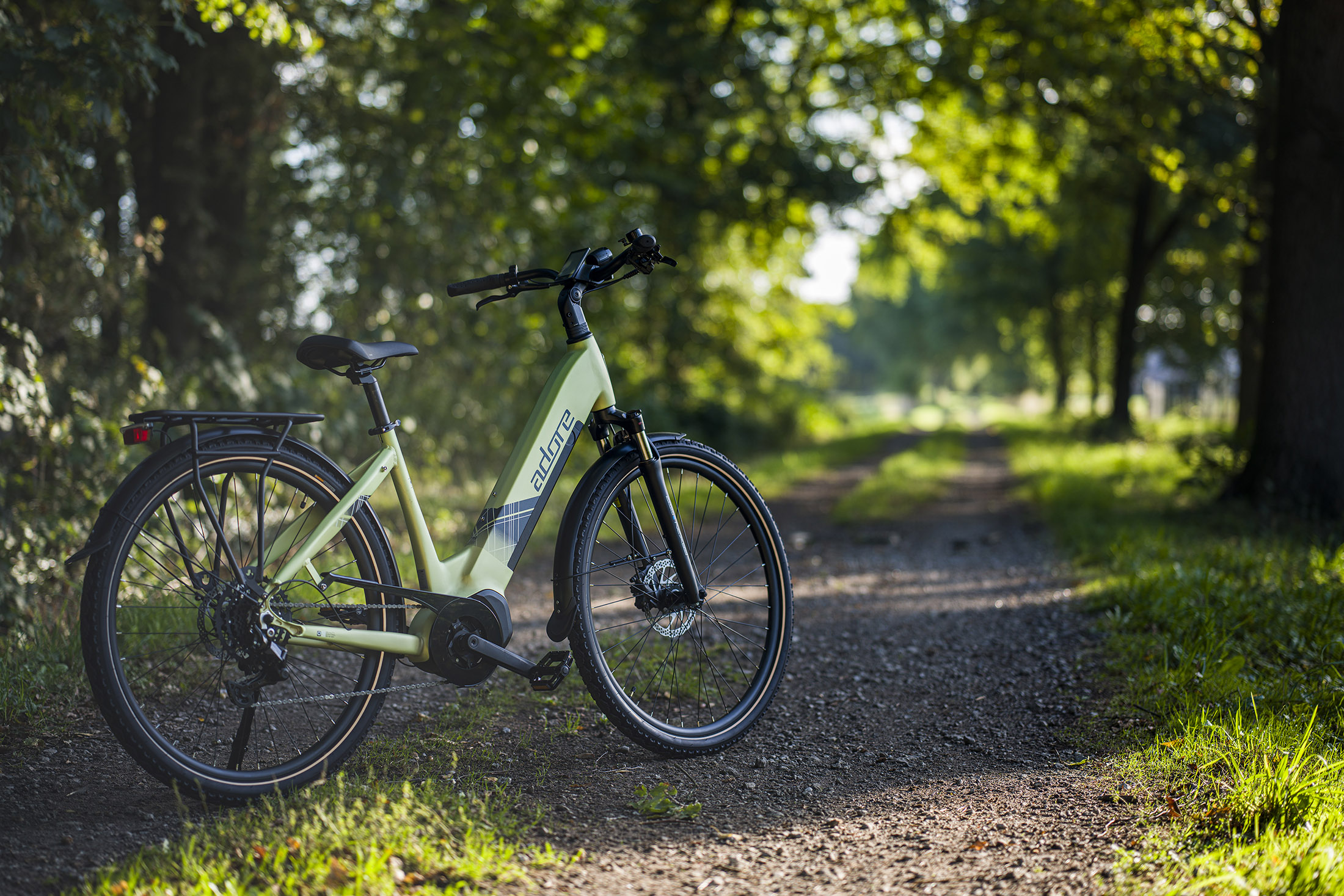 Grünes Adore-Elektrofahrrad auf einem Schotterweg, Bäume im Hintergrund, sonniger Tag.