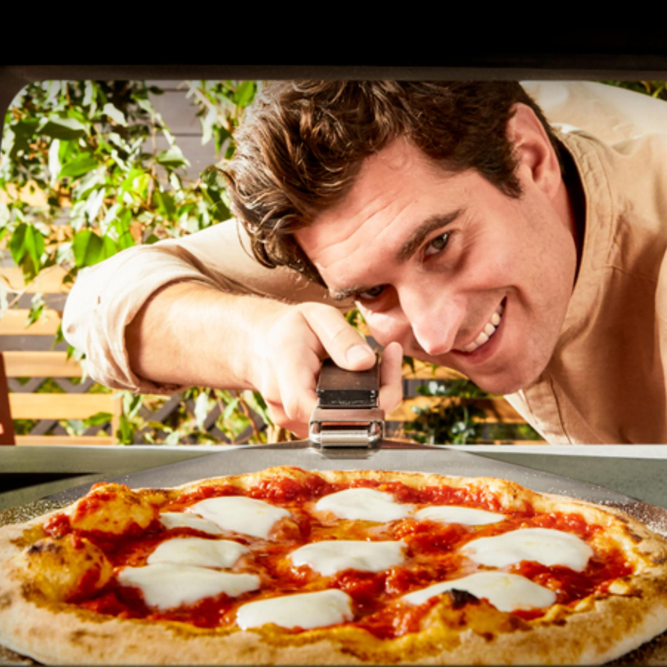 Ein Mann lächelt eine Pizza an. Pizza hat Käse und Soße. Der Mann hält einen Pizzaschieber.