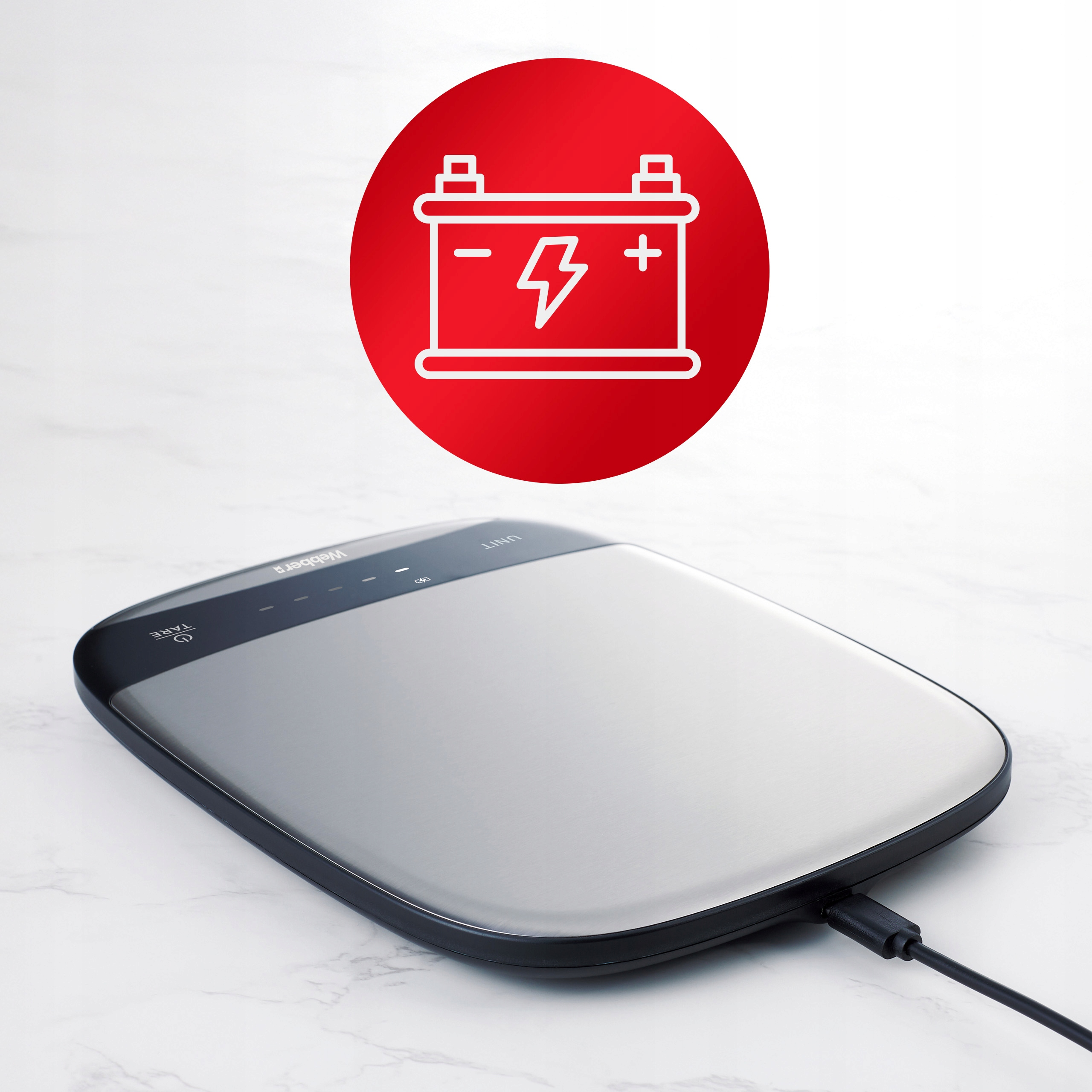 Waga cyfrowa z czerwonym okręgiem zawierającym ikonę baterii. Waga jest srebrno-czarna, z kablem.