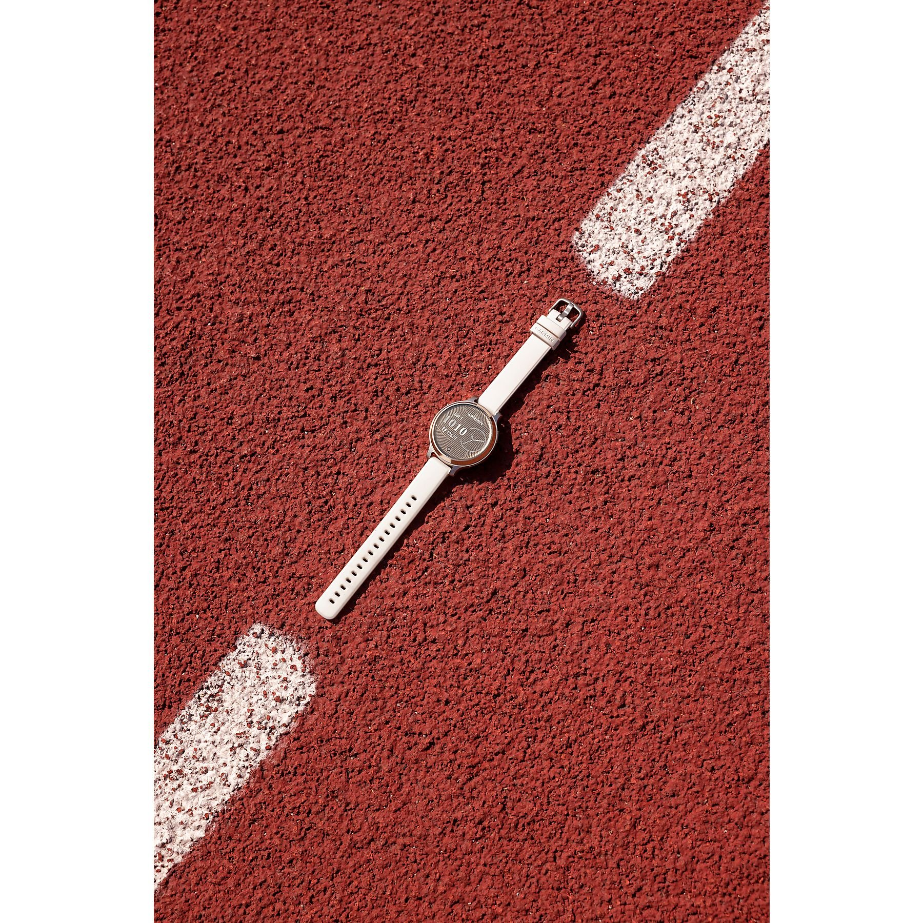 Eine weiße Smartwatch liegt auf einer roten Laufstrecke in der Nähe einer weißen Linie. Die Uhr zeigt die Zeit.