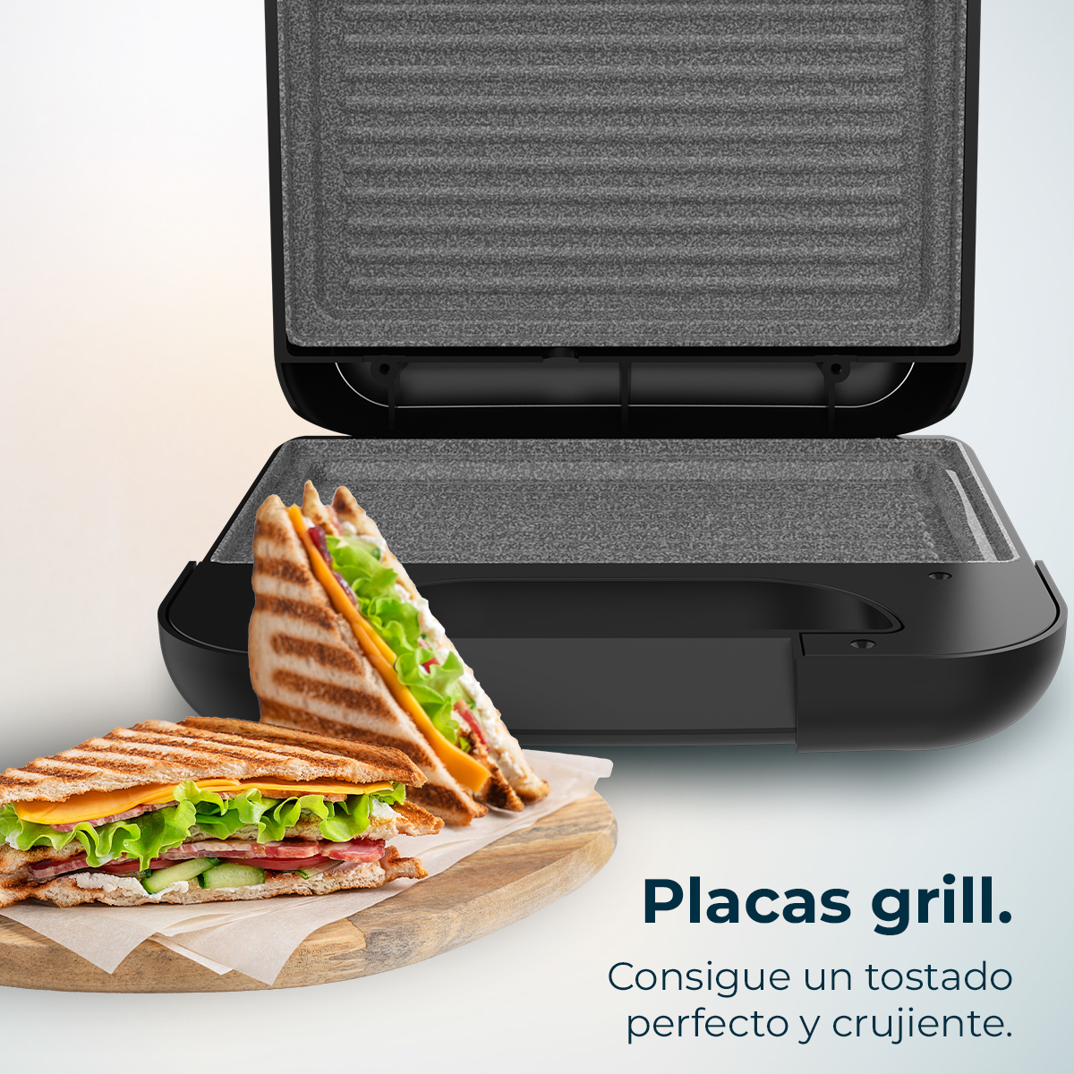 Una griglia per sandwich con due sandwich davanti. Uno è su un tagliere di legno. La griglia è aperta.