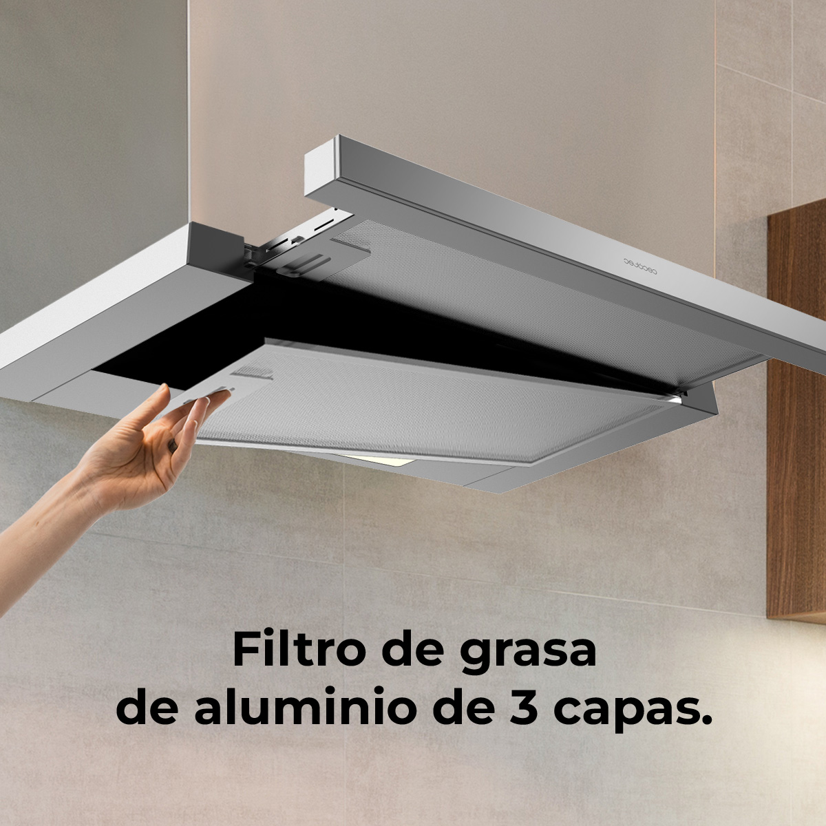 Una mano levanta un filtro de grasa de aluminio de una campana extractora. El filtro es de tres capas. El fondo muestra una pared de cocina.