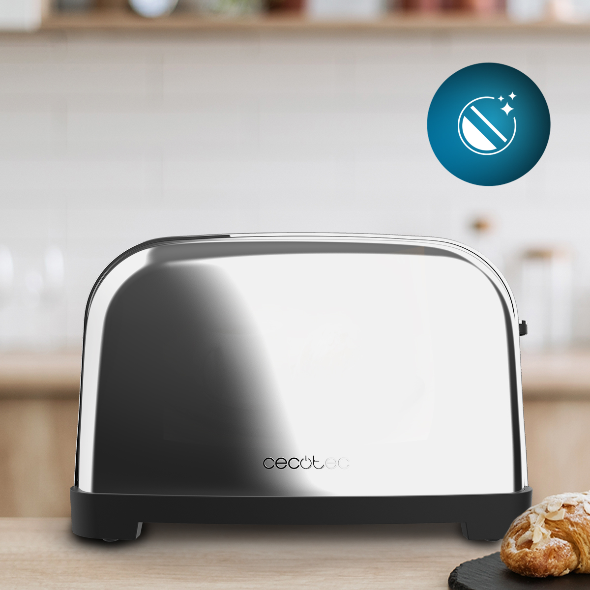 Błyszczący chromowany toster z czarną podstawą stoi na drewnianym blacie. Obok rogalik. Niebieska ikona wskazuje na łatwe czyszczenie.