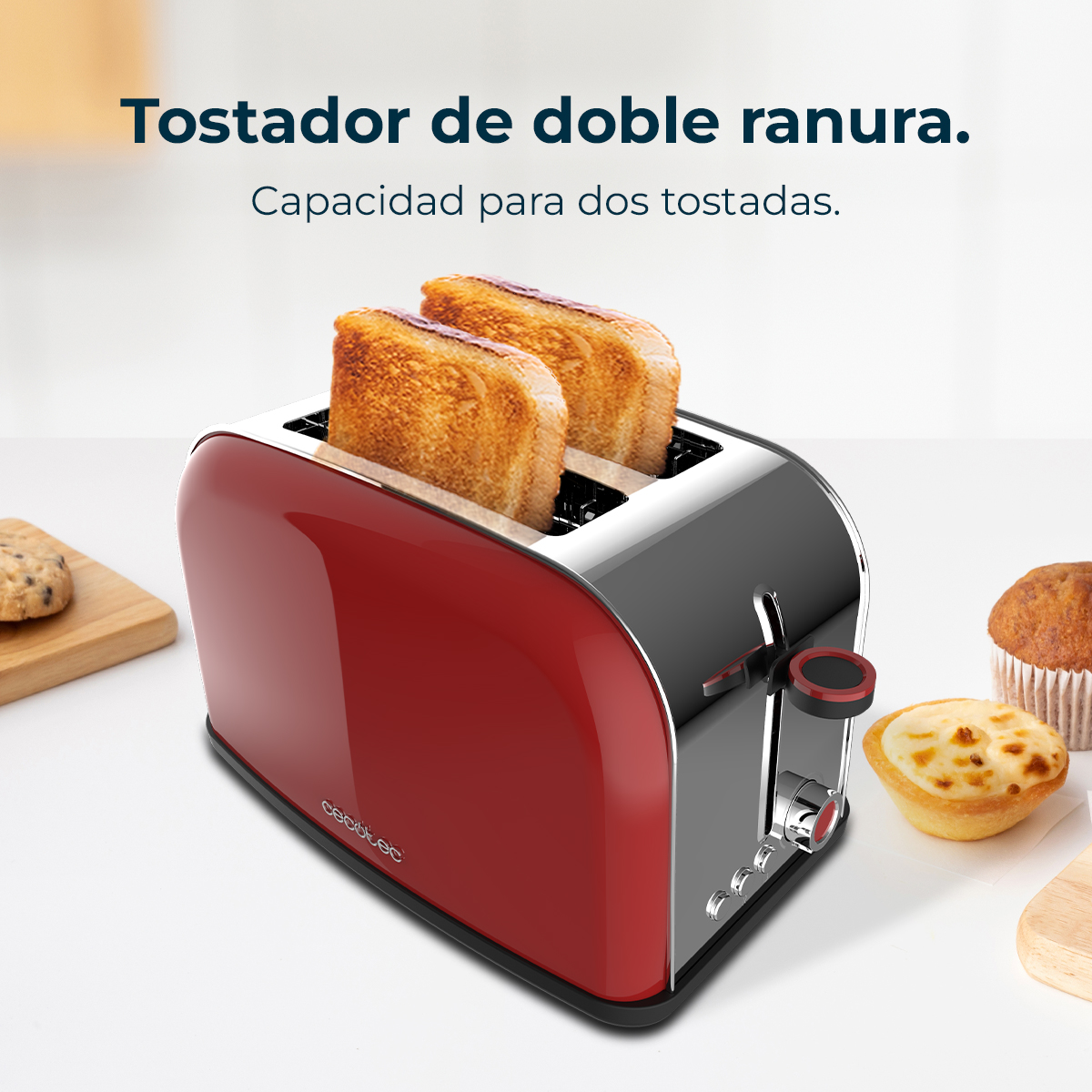 Una tostadora roja y plateada con dos rebanadas de pan tostado. Hay pasteles en el lateral sobre una superficie blanca.