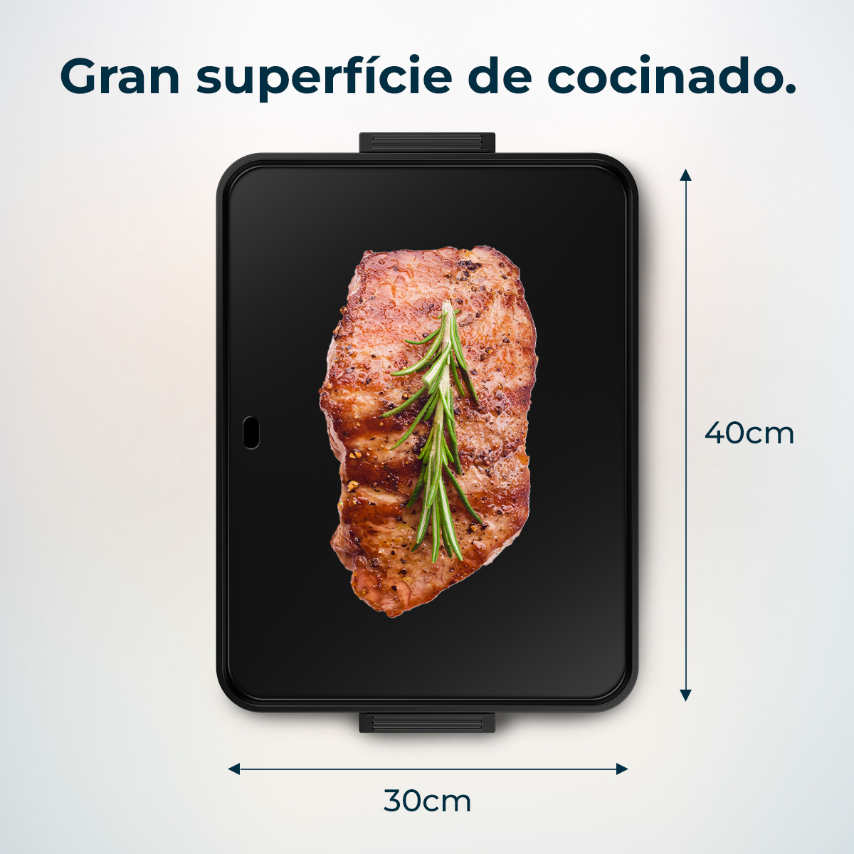 A cooked steak with rosemary on a black cooking surface. It is 40cm x 30cm. Text says: Gran superficie de cocinado.