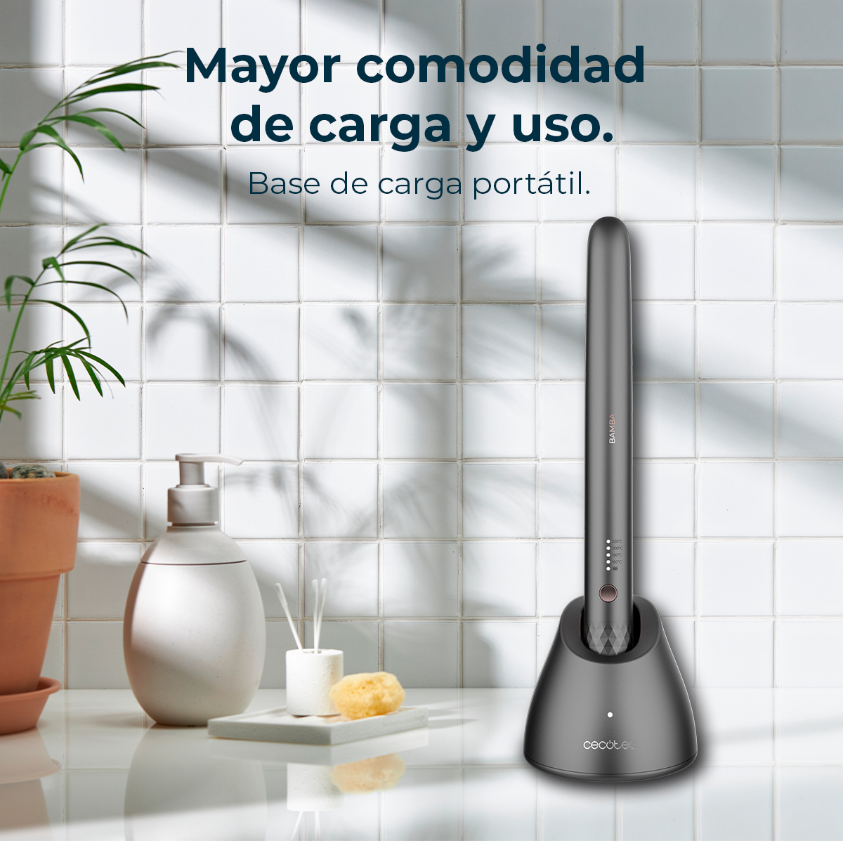 Szare narzędzie do stylizacji włosów w stacji ładującej stoi na białej powierzchni. Widoczna jest również roślina, dozownik mydła i gąbka.