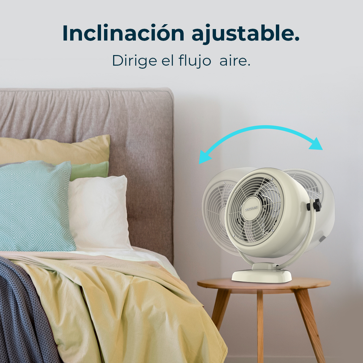 Un ventilatore beige su un tavolino di legno vicino a un letto con cuscini e una coperta. Il ventilatore oscilla con frecce.