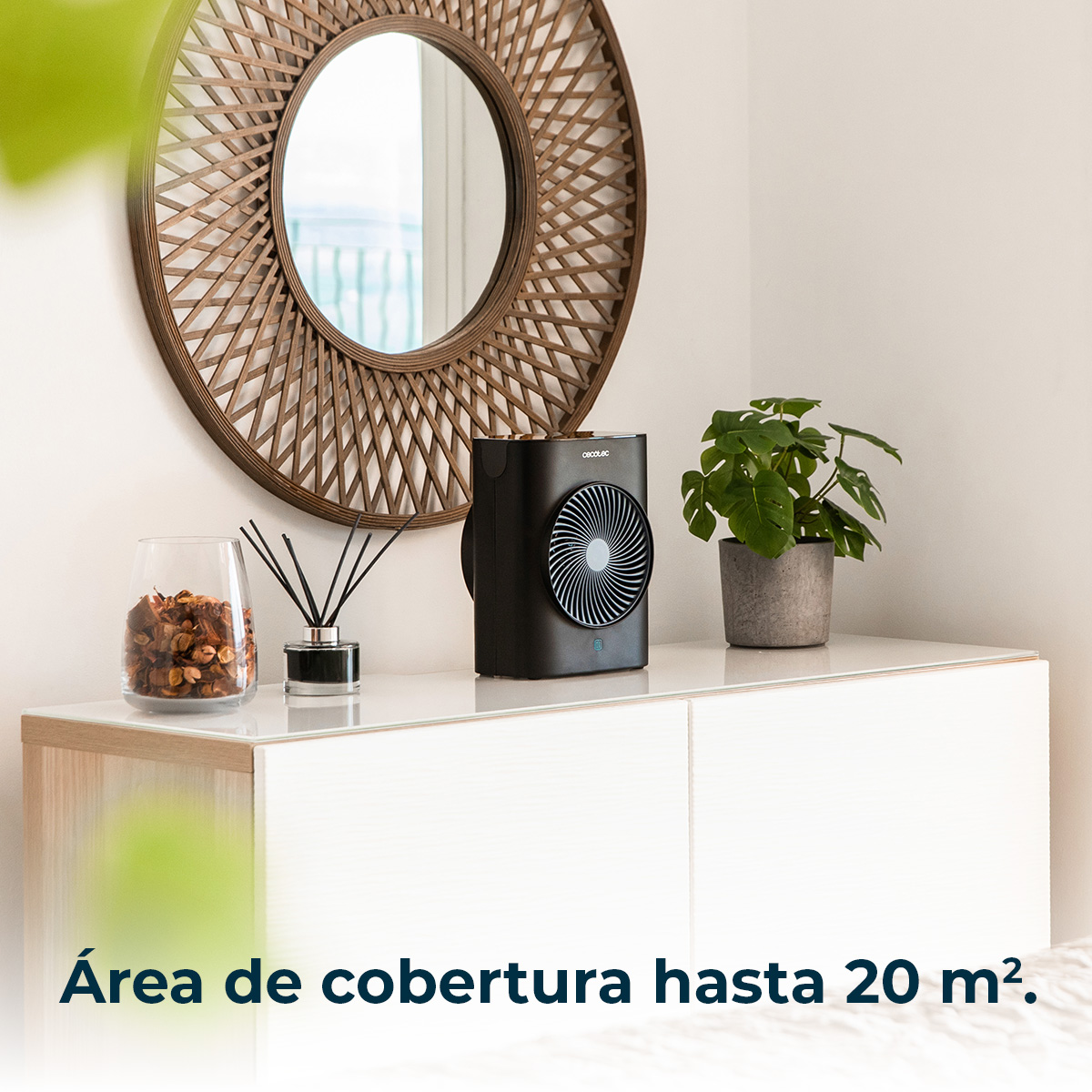 Un ventilatore nero, una pianta e decorazioni su un mobile bianco. Uno specchio rotondo è appeso sopra.