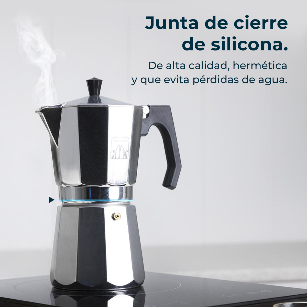 Una cafetera moka plateada con asa negra sobre una vitrocerámica. Sale vapor de la cafetera. Texto en español sobre el sello de silicona.