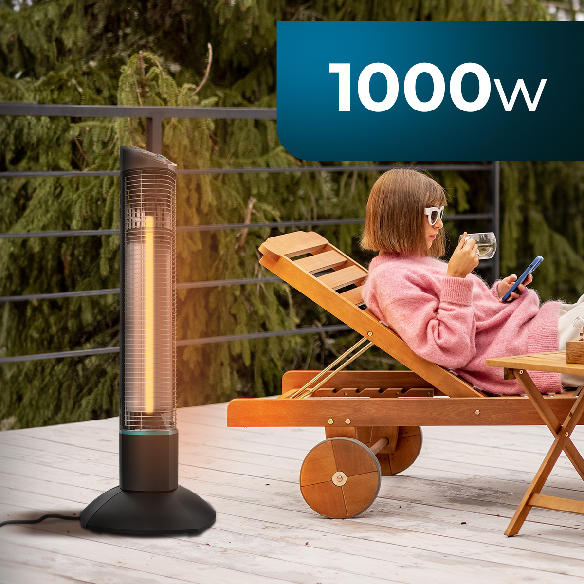 Kobieta w różowym swetrze, okularach przeciwsłonecznych, siedzi na leżaku, trzymając telefon i filiżankę. Po lewej stronie znajduje się grzejnik. Znak 1000w.