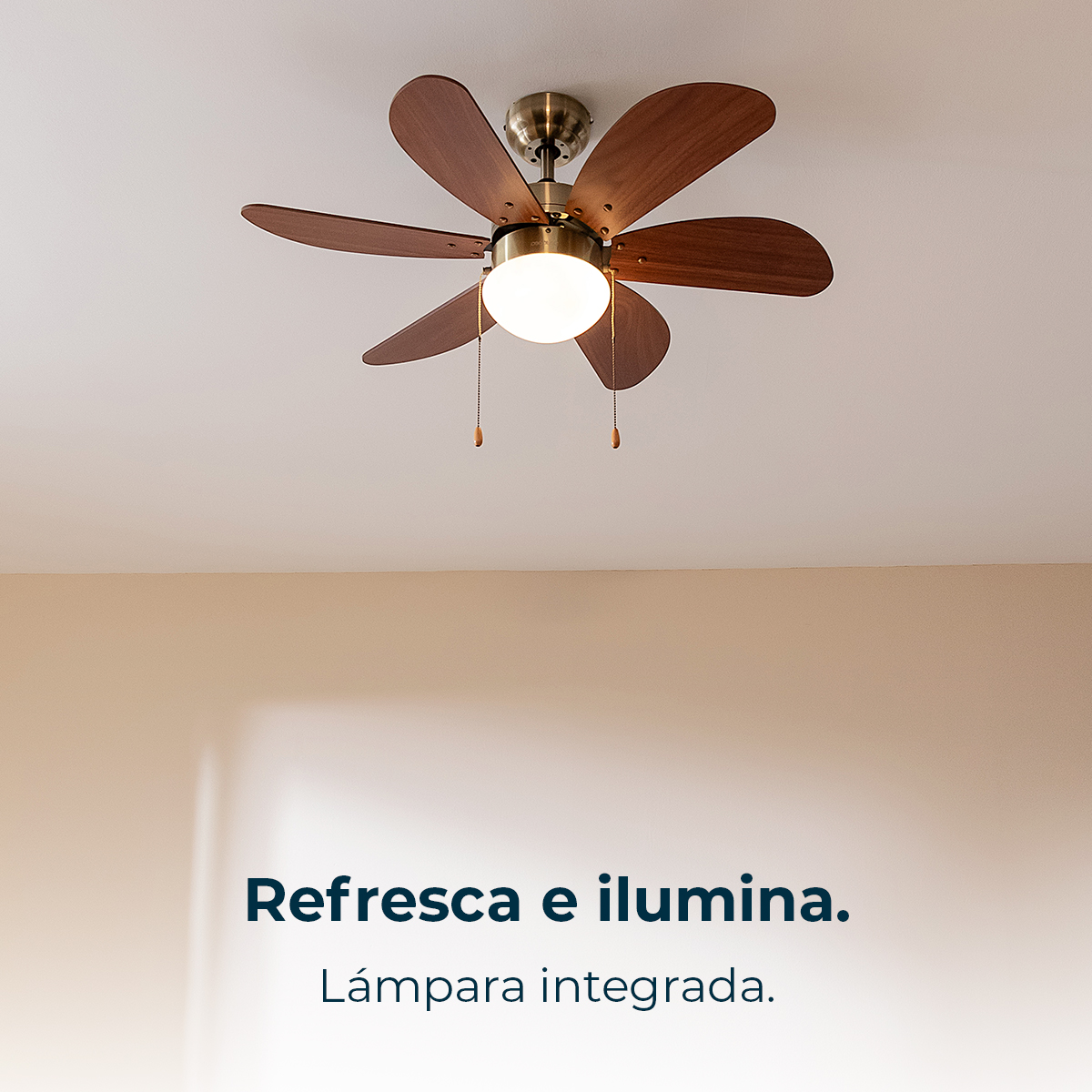 Un ventilador de techo con aspas de madera y una lámpara cuelgan de un techo blanco. Las paredes son de color beige claro.