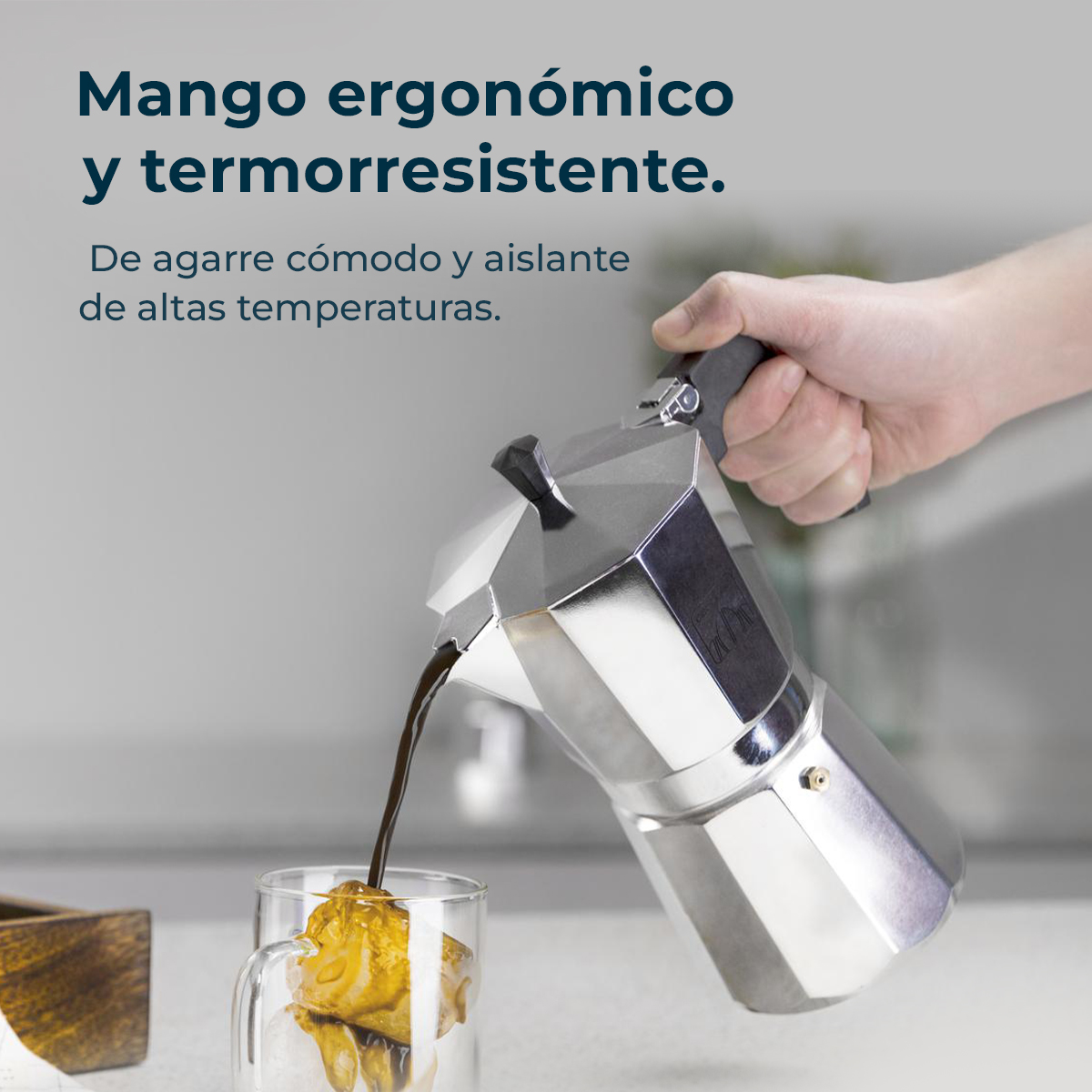 Una mano versa il caffè da una moka argentata in un bicchiere con cubetti di ghiaccio. Testo: Manico ergonomico e resistente al calore.