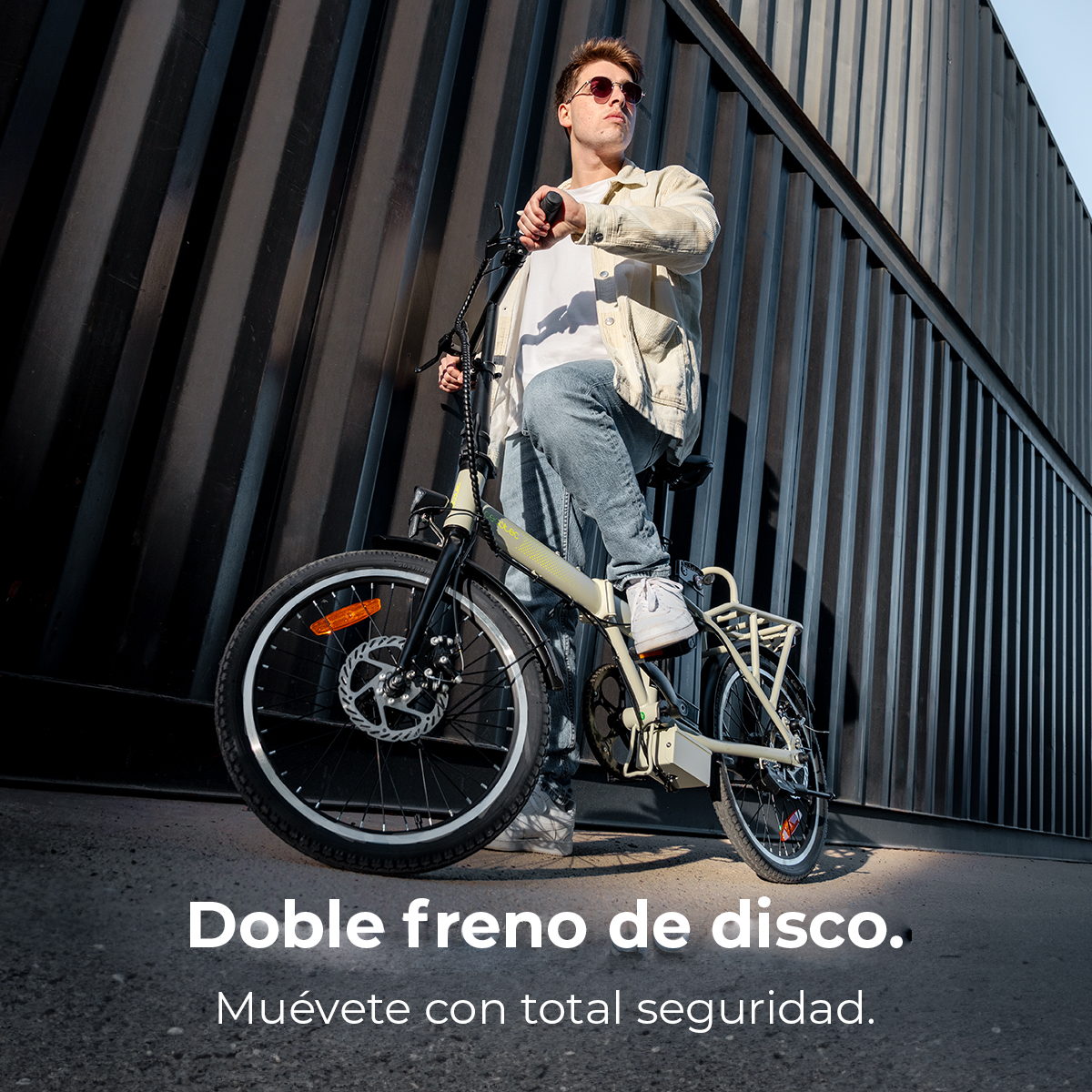 Un uomo con occhiali da sole e giacca, accanto a una bici elettrica con freni a disco. Dietro, un muro di metallo nero.
